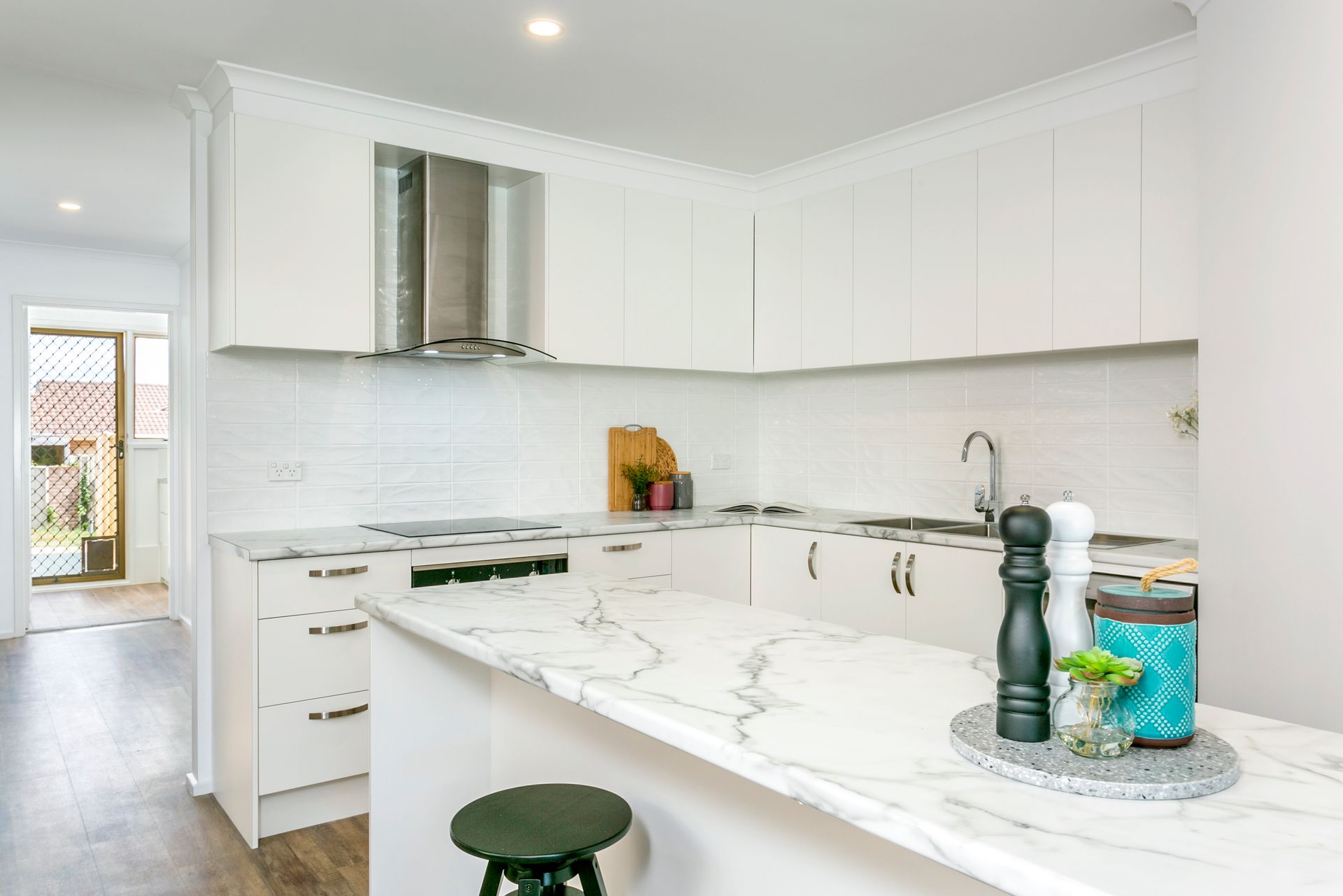 White kitchen with marble countertop, stainless steel range hood, and wooden floors.
