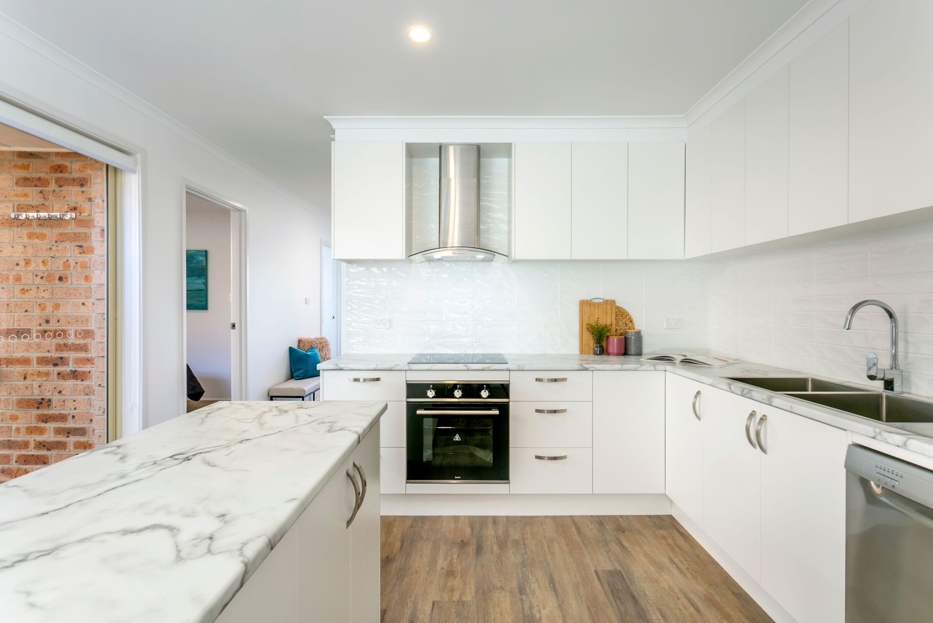 Modern white kitchen with marble countertops, stainless steel appliances, and wooden flooring.