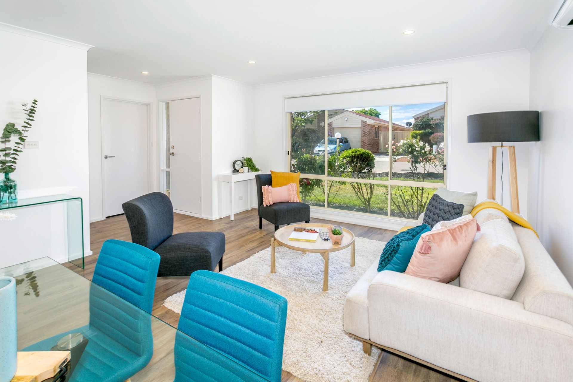 Living room with white walls, window, furniture in blues, grays, yellow, pink, and brown tones.