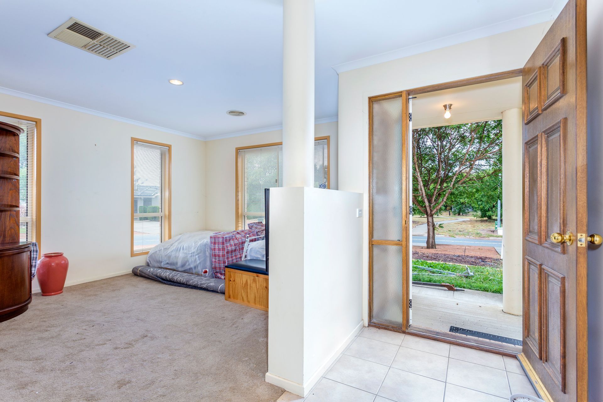 Interior entryway with open wooden door, tiled floor, carpeted living area, and a view of a tree outside.