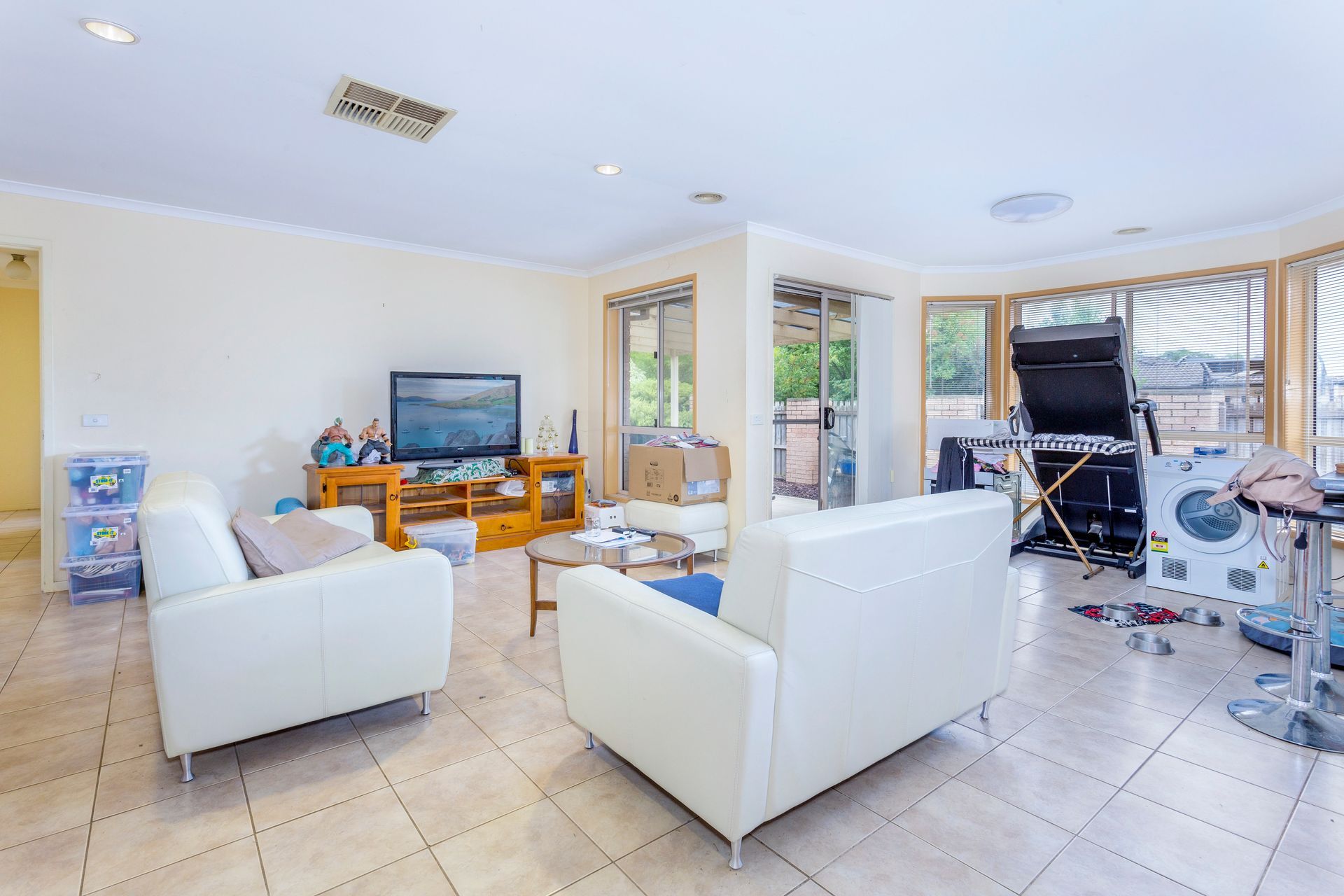 Living room with white couches, TV, and miscellaneous items scattered about.
