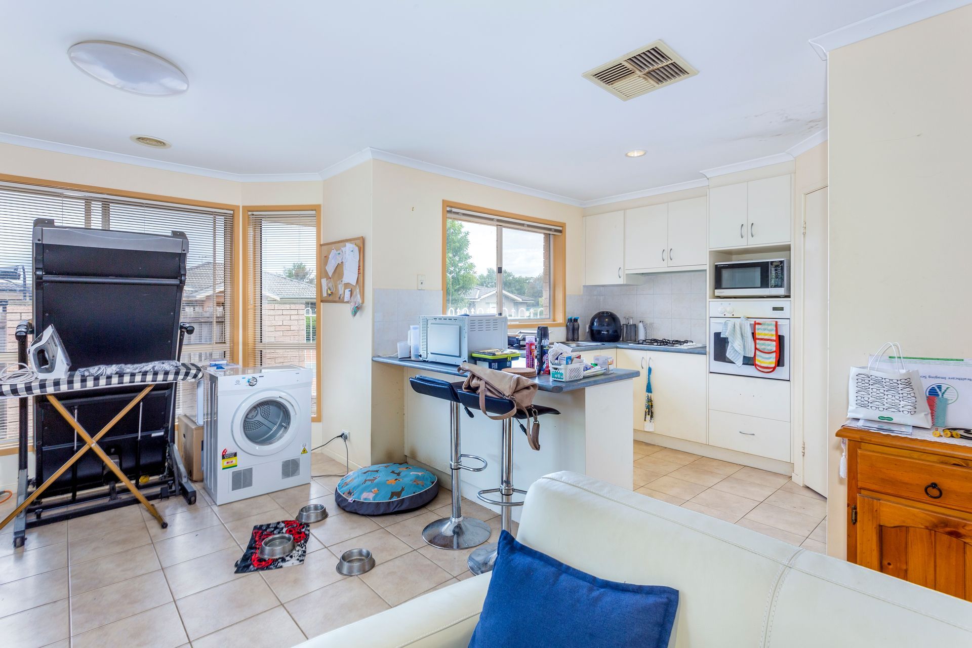 Interior view of a kitchen and living area, with a washing machine and clutter visible.