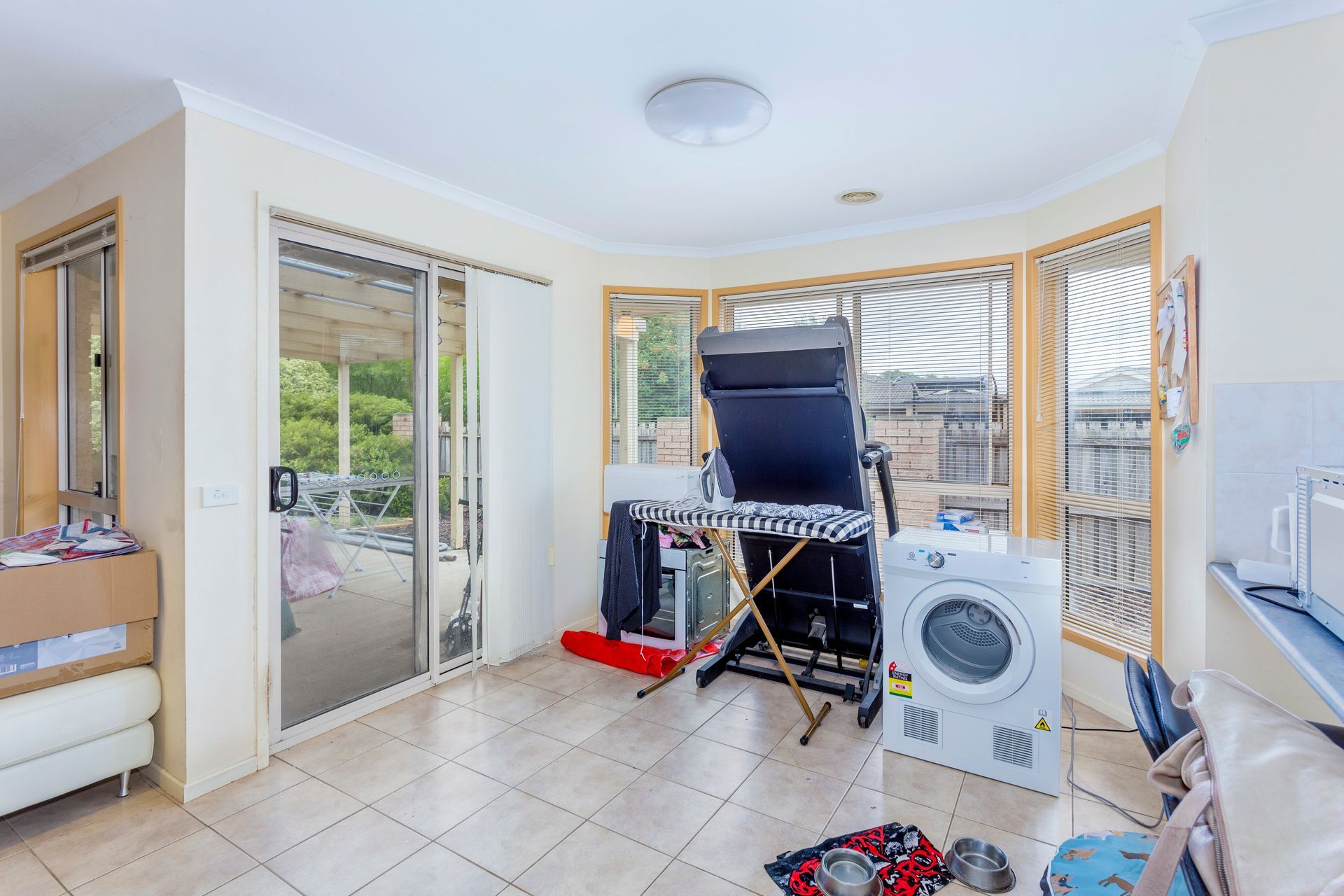 Bedroom with bed, stacked cushions, window, and small cabinet.