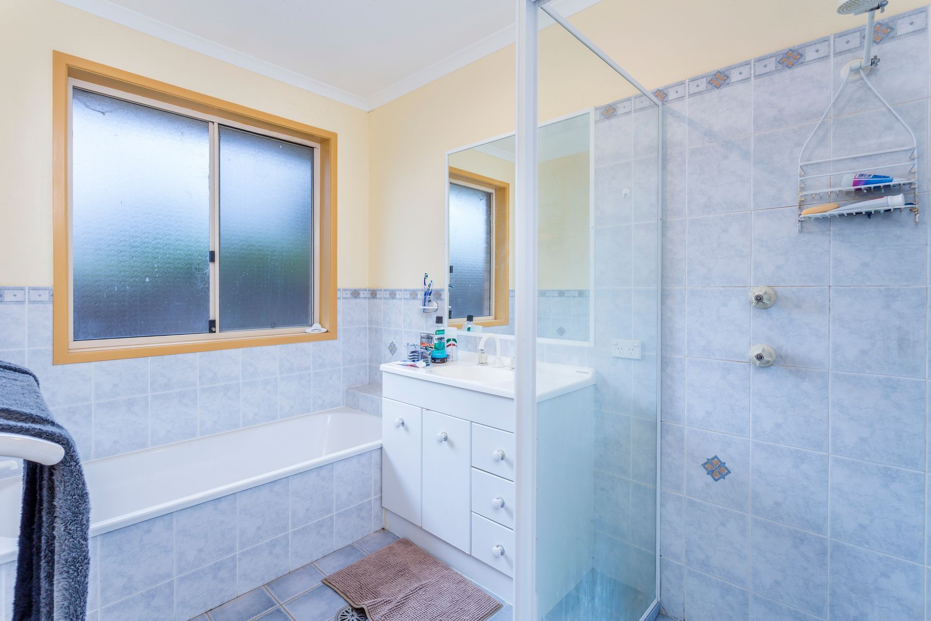 Bathroom with tub, shower, and vanity. Pale blue tiled walls, window, and neutral tones.