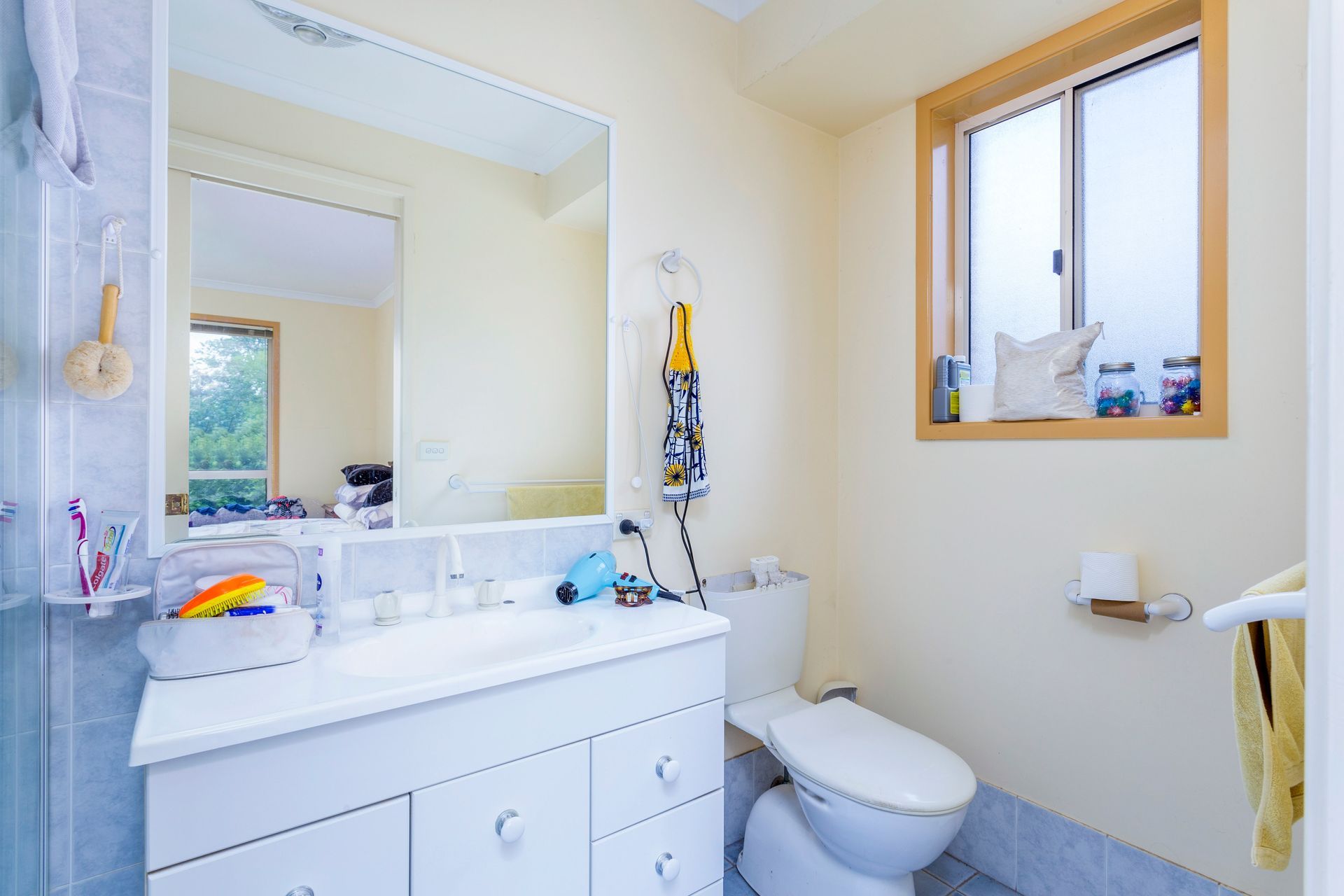 Bathroom with tub, shower, and vanity. Pale blue tiled walls, window, and neutral tones.