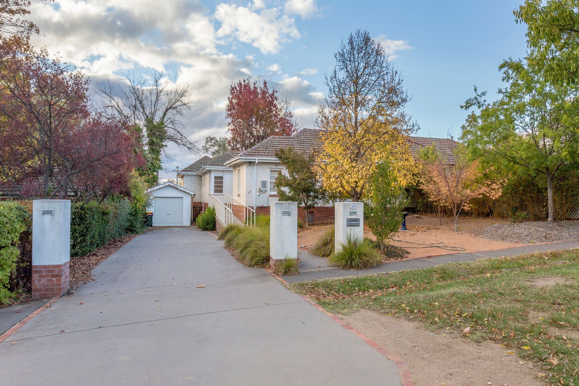 Driveway leading to a white house with pillars, surrounded by trees with fall foliage.