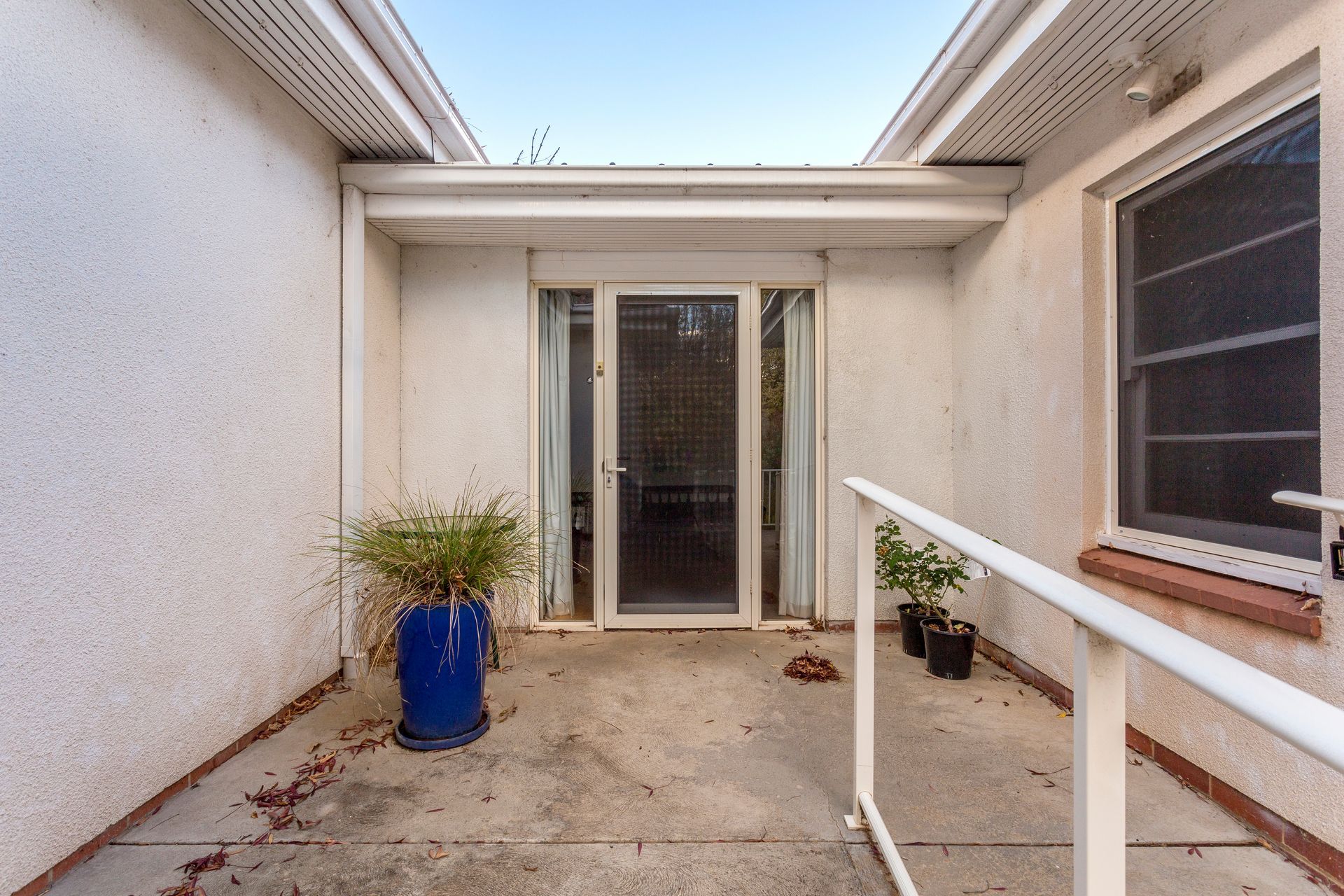 A small outdoor patio with a blue planter, sliding glass door, and a white handrail.