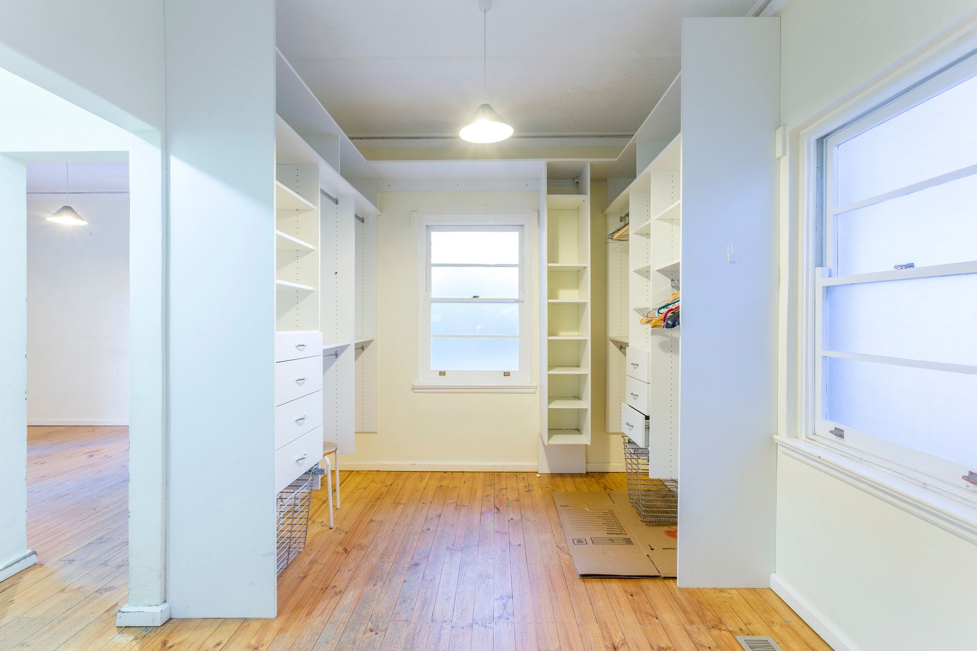 Walk-in closet with white shelves and drawers, a window, and wood flooring.