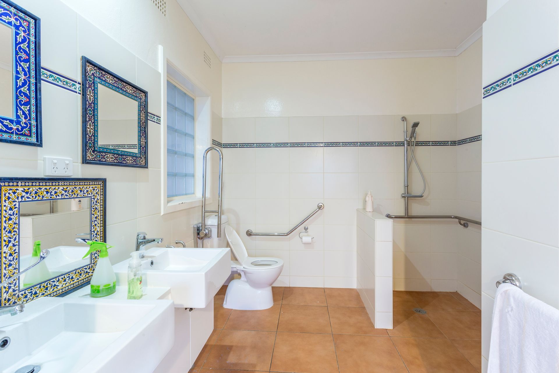 Accessible bathroom with grab bars, roll-in shower, and low sink, tiled walls, and decorative mirror frames.