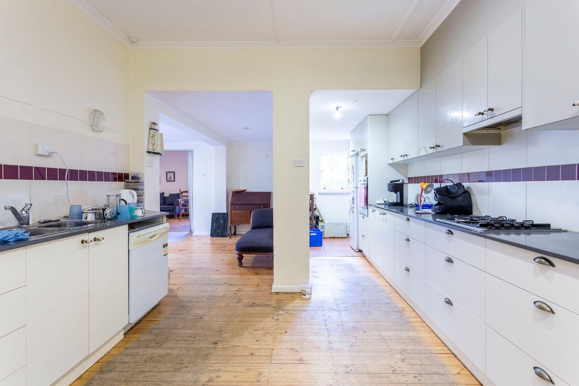Kitchen with white cabinets, dark countertops, and light wood floor. Open doorway leads to another room.