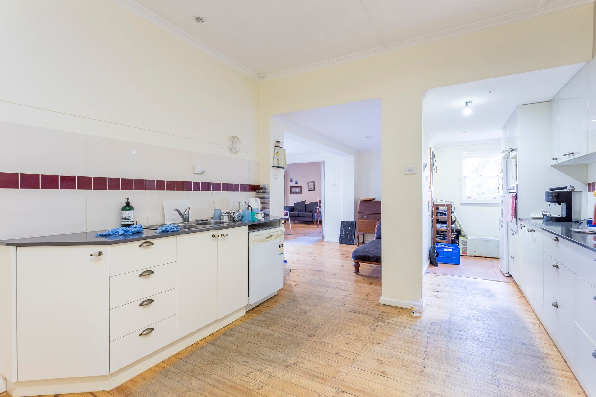 Kitchen with white cabinets, dark countertops, and light wood floor. Open doorway leads to another room.