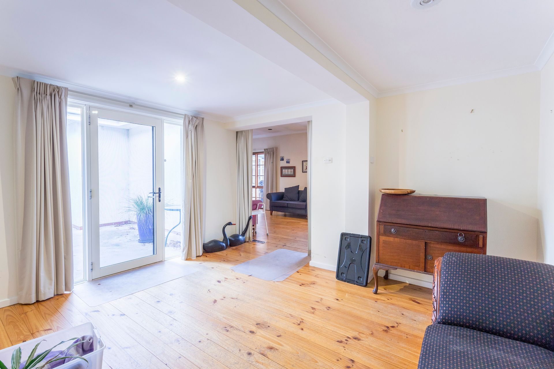 Spacious room with wooden floors, leading to a patio and another room with a couch.