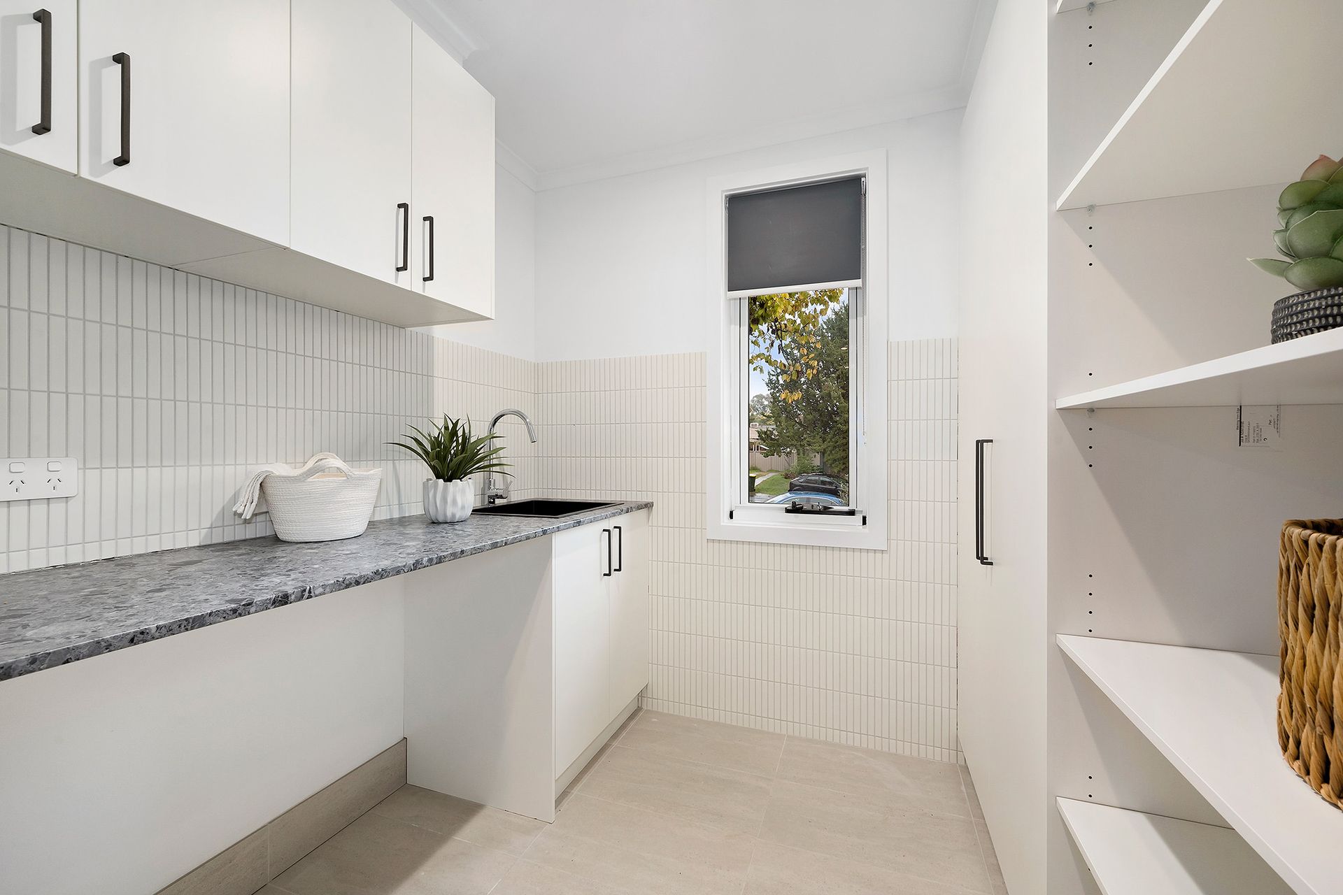 White laundry room with cabinets, counter, window, and shelves.