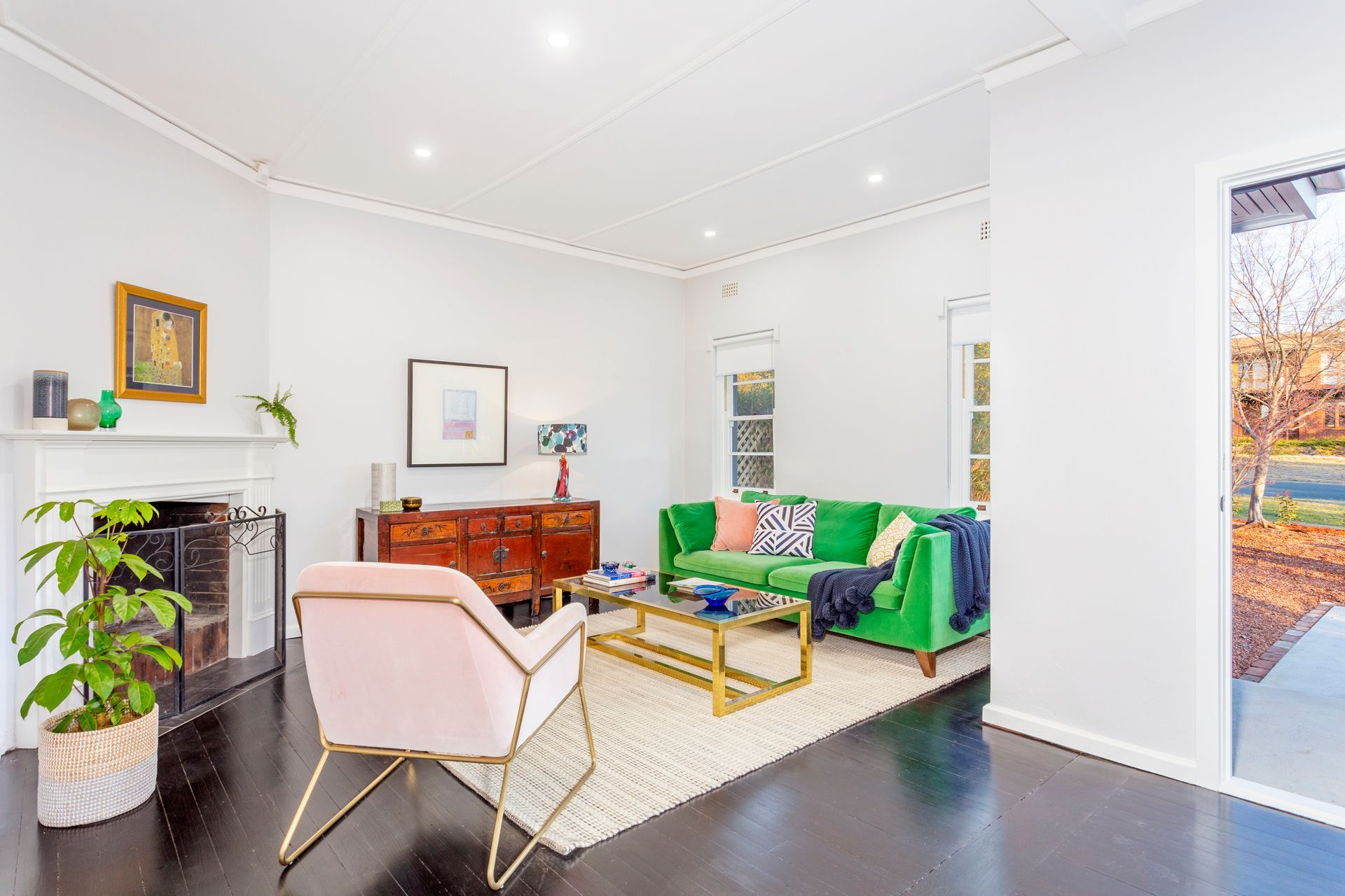 Living room with green sofa, pink chair, fireplace, and dark wood floors.