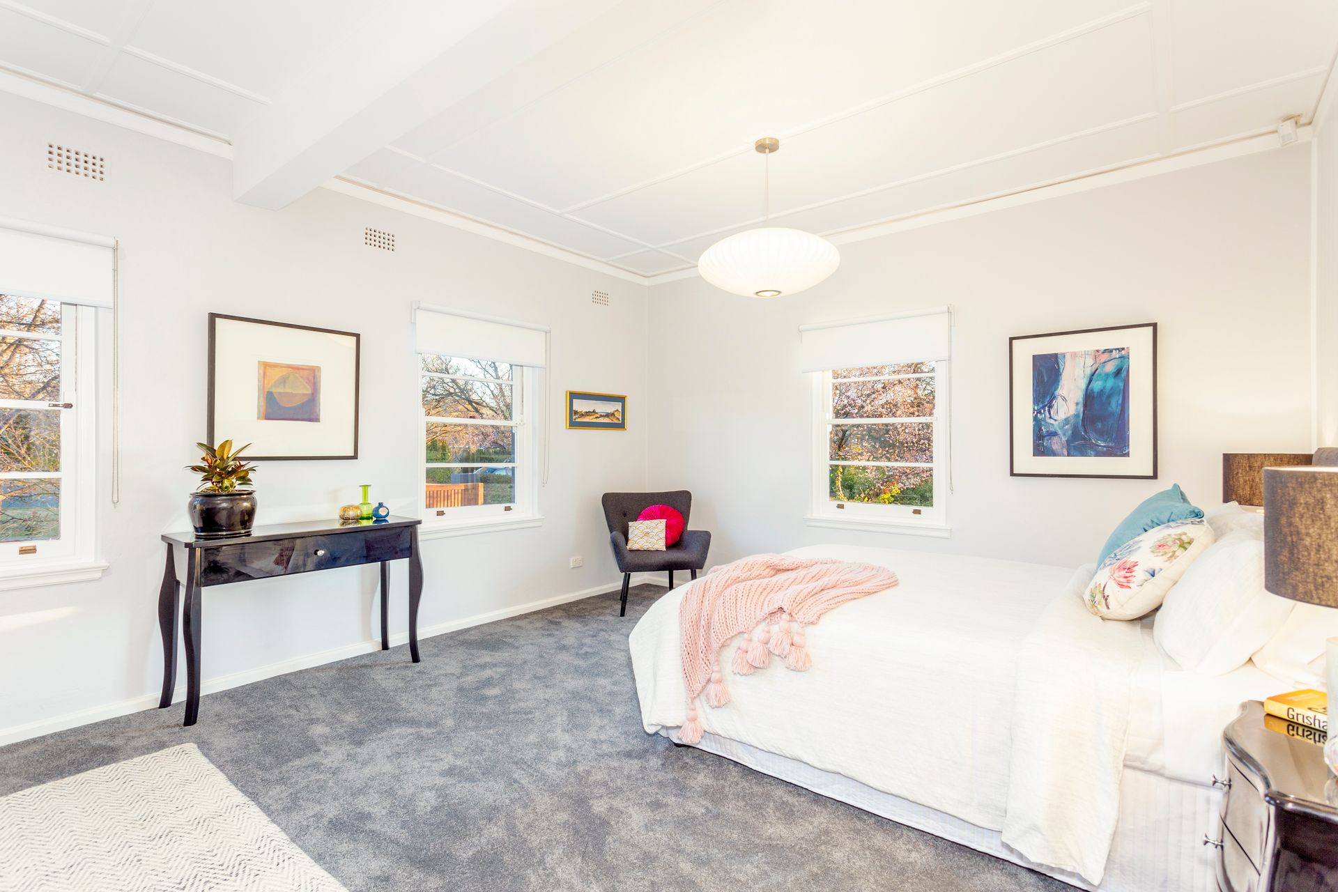 Bedroom with white walls, windows, bed, artwork, and a dark desk.