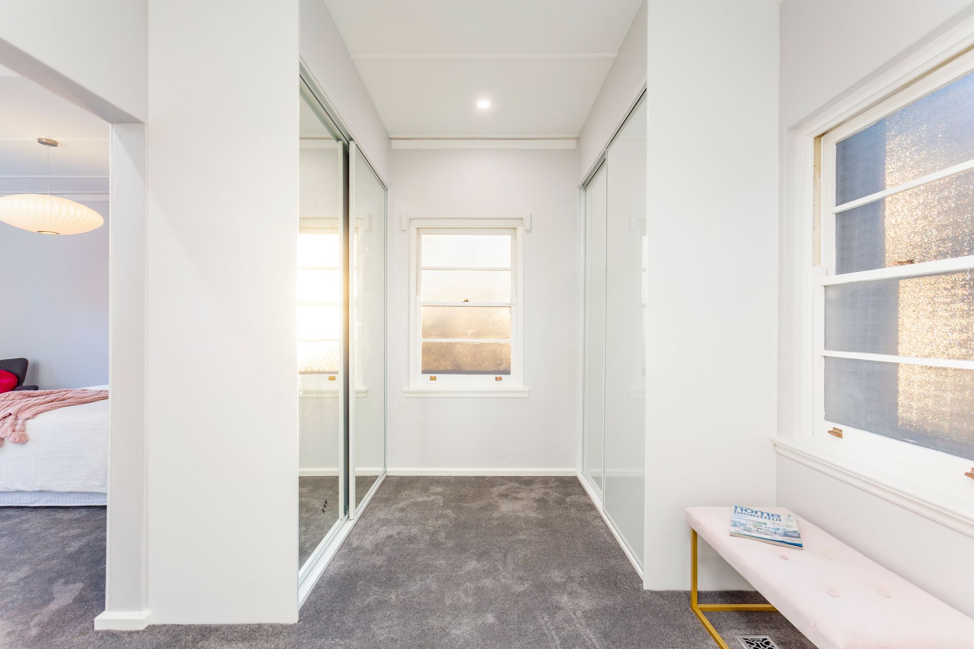 Bright bedroom with white walls, bed, windows, artwork, and black furniture.