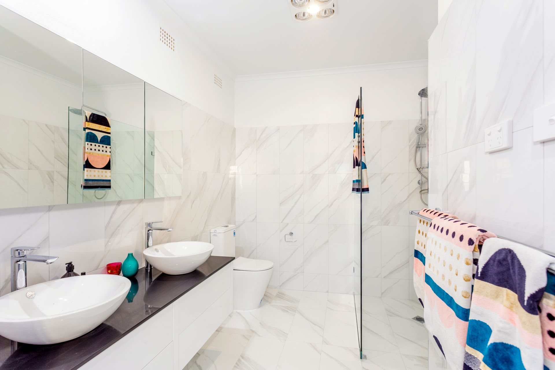 Modern bathroom with marble walls, double sinks, and colorful towels.