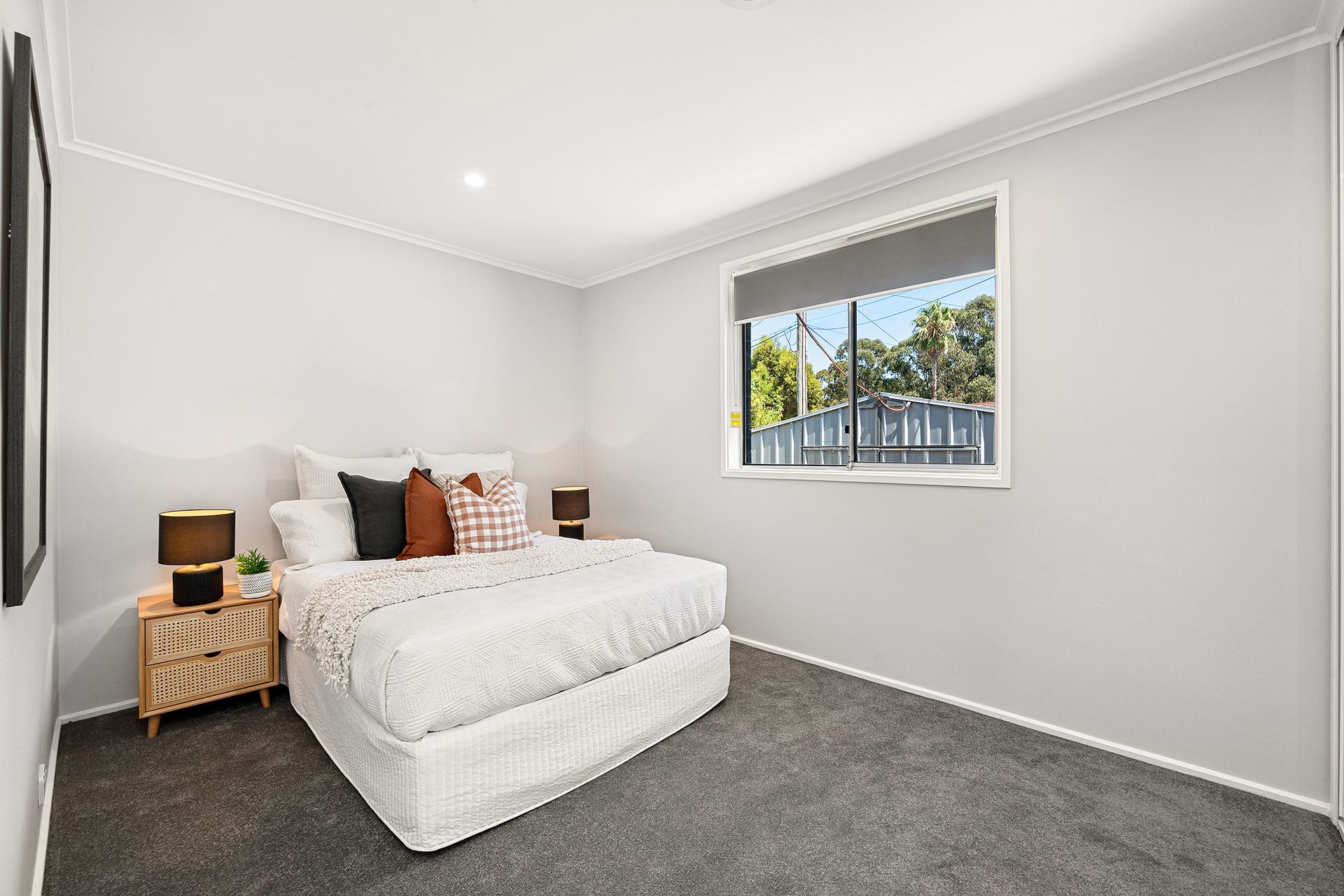 Bedroom with a bed, two bedside tables, a window, and gray carpet.