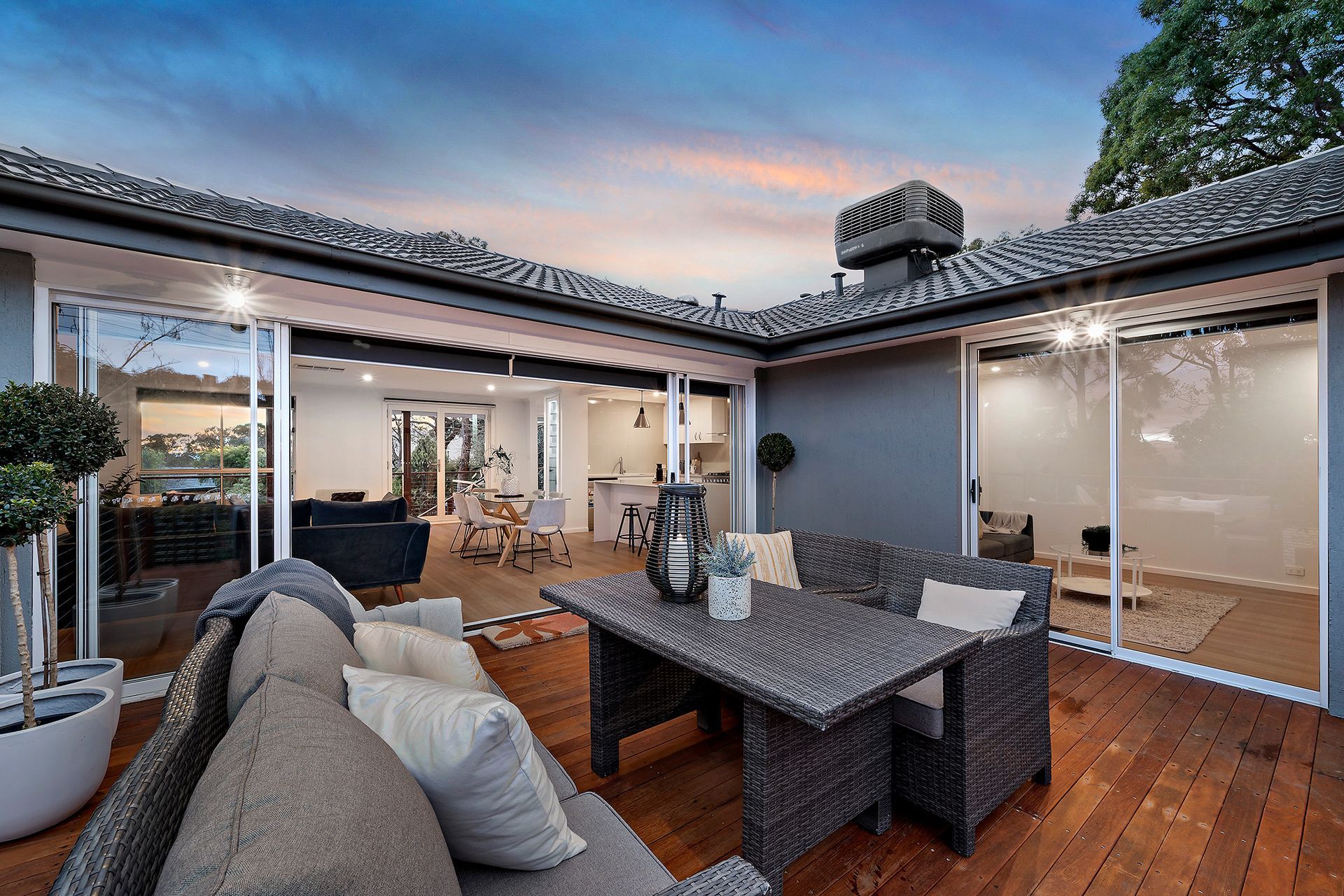 Patio with gray wicker furniture, sliding doors, and a wood deck. Evening sky.