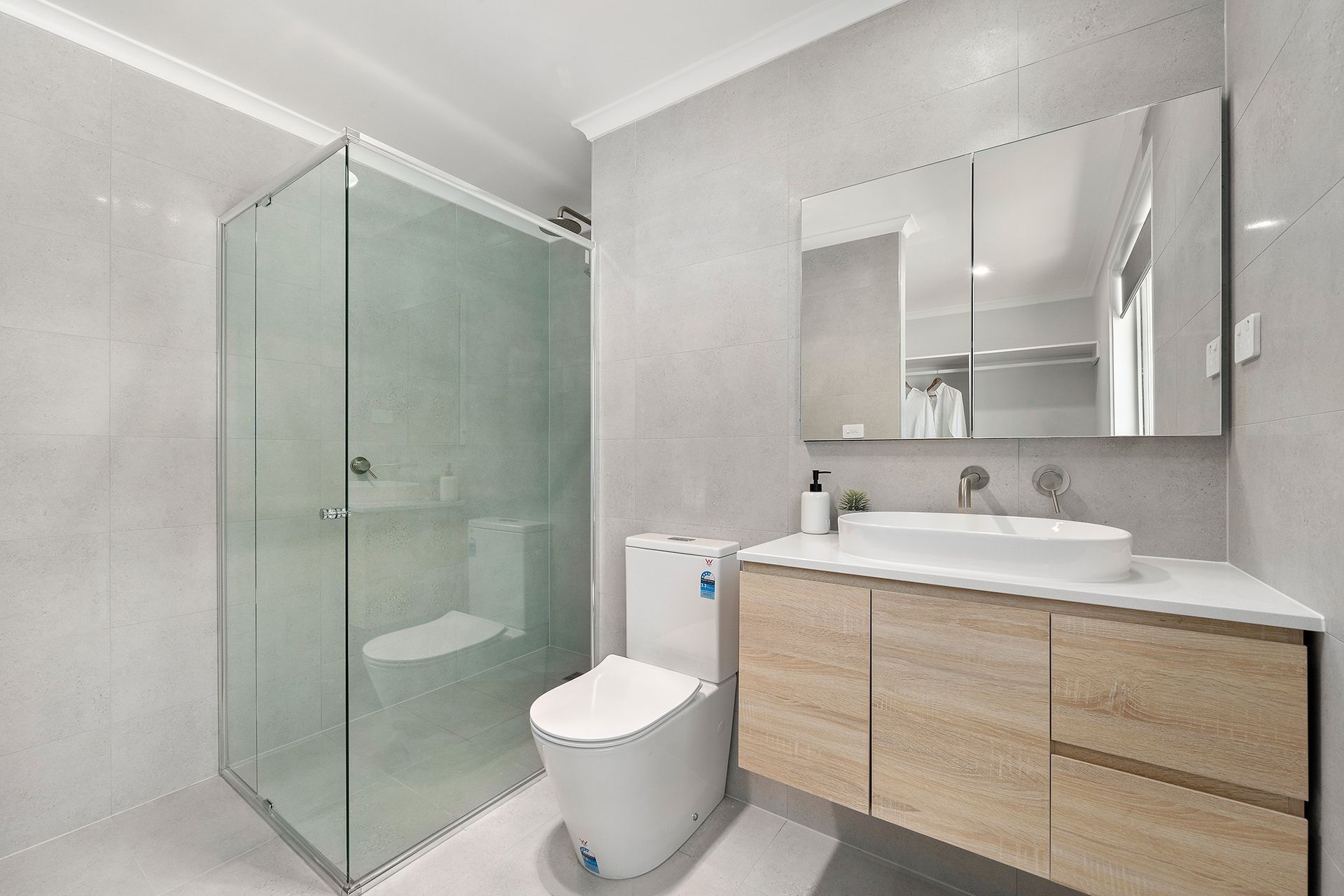 Modern bathroom with a glass shower, toilet, and wooden vanity with a sink.