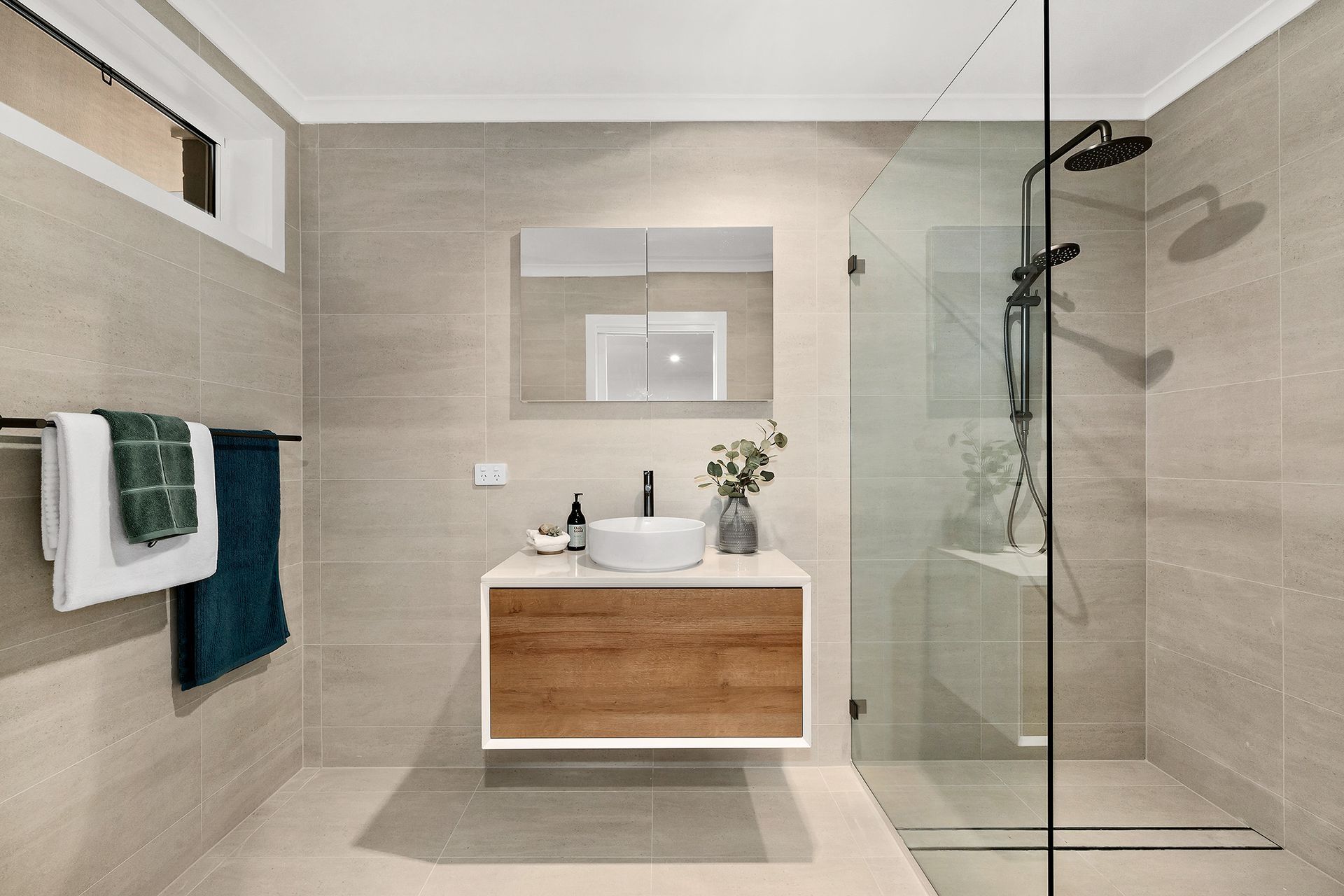 Modern bathroom with wood vanity, glass shower, and neutral tile.