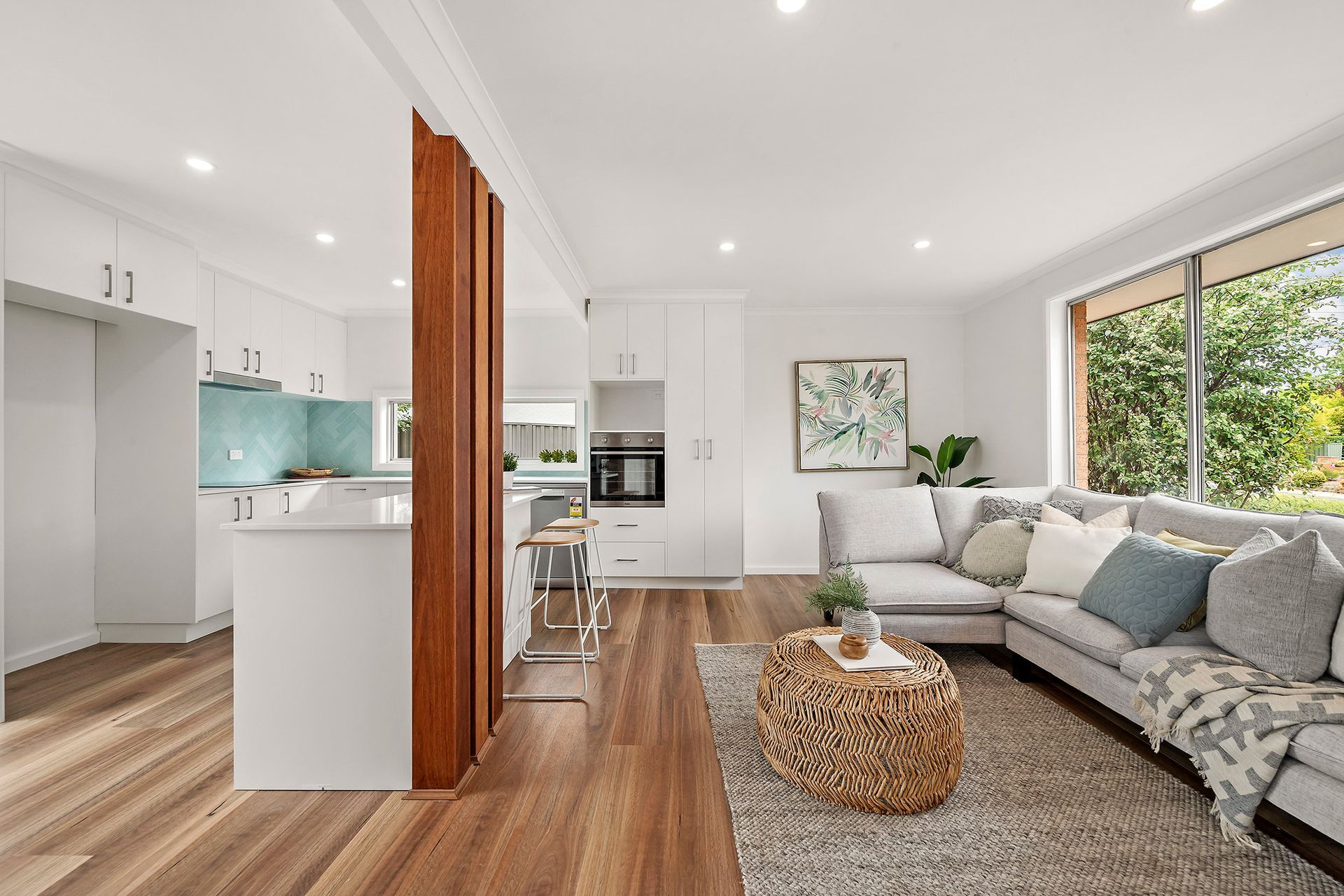 Open-concept living space with kitchen and living room. Wooden floors, white cabinets, and a gray sectional.