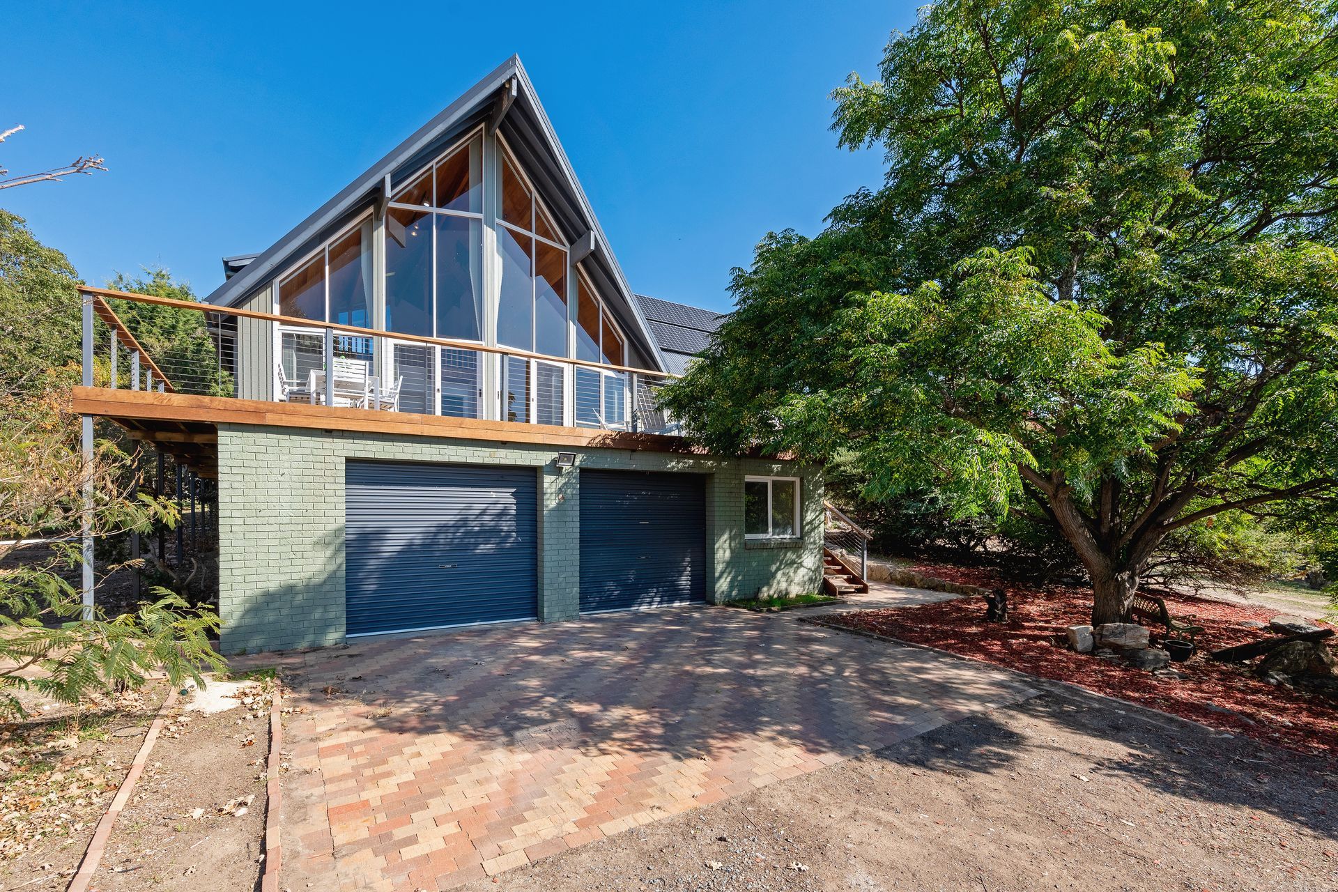 A-frame house with glass windows and garage, next to a tree and driveway on a sunny day.