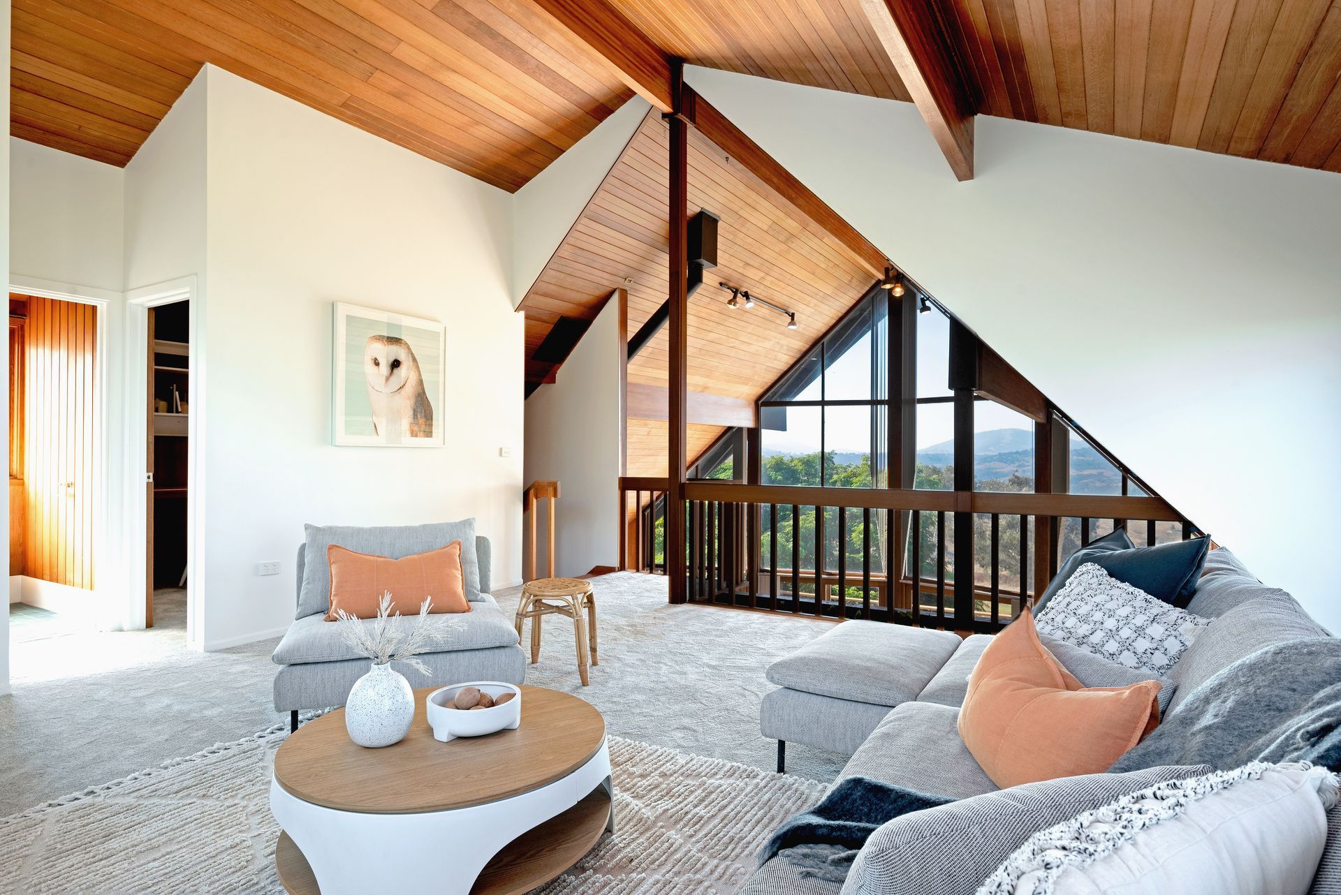 Living room with vaulted wood ceiling, light-colored walls, gray furniture, and a view through a large window.