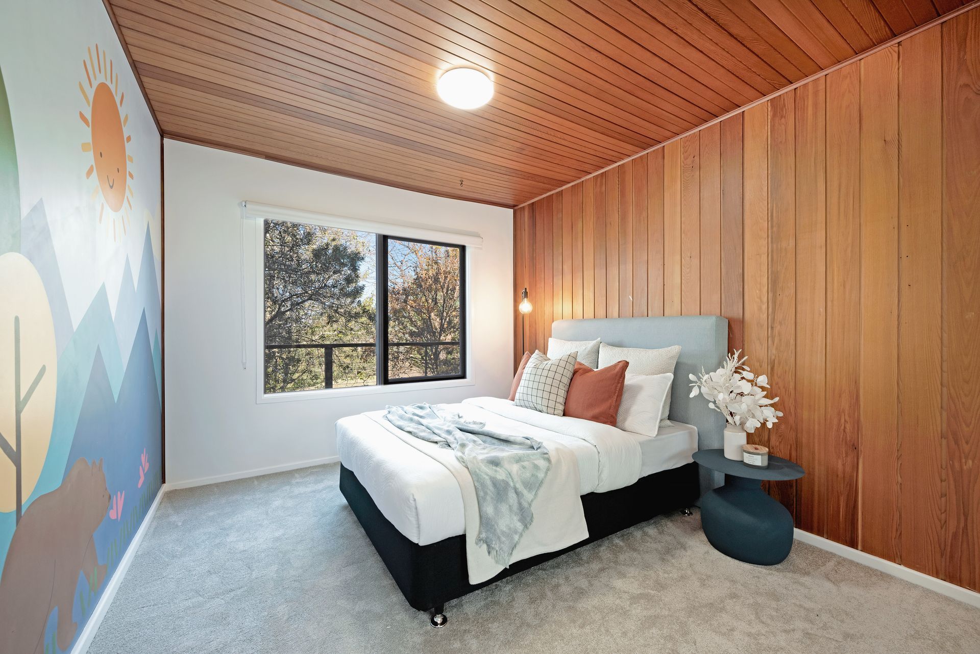 Bedroom with wood paneling, a mural, and a bed with pillows.