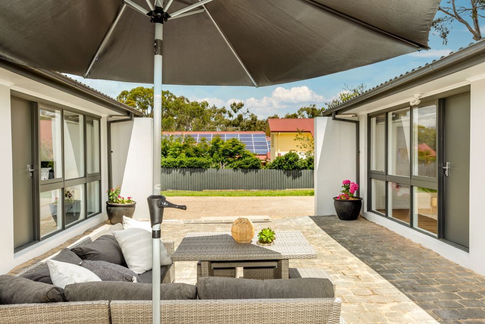 Patio with grey furniture under a black umbrella, flanked by two white buildings.