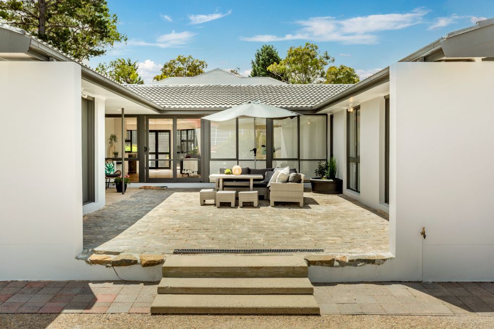 Courtyard with outdoor seating, a white umbrella, and steps leading to the area. Gray and white walls, blue sky.