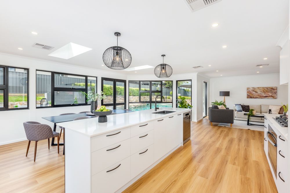 Bright white kitchen with large island, black-framed windows, wood flooring.