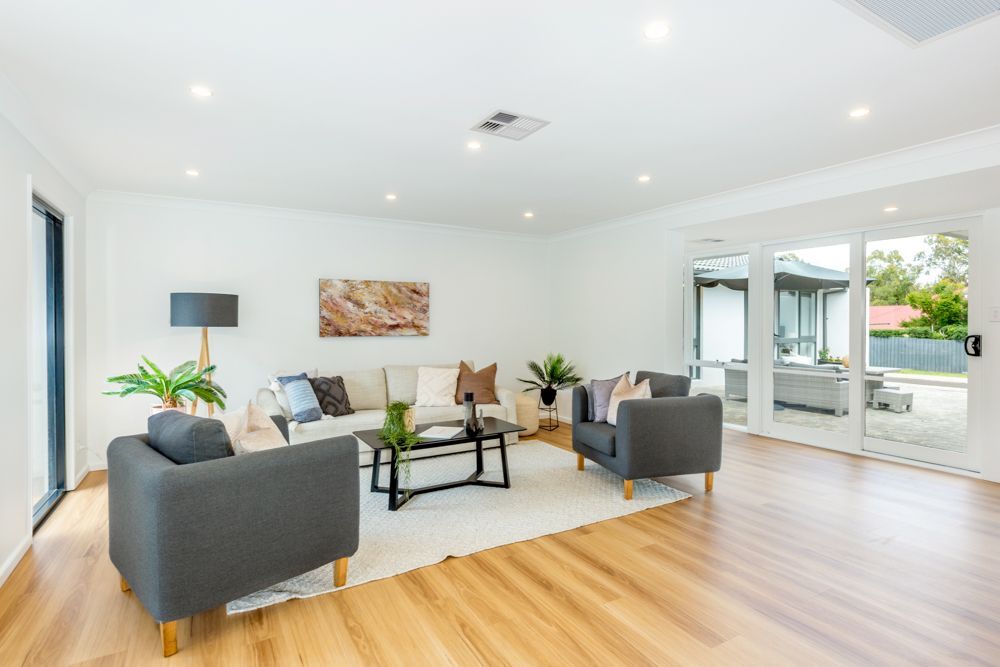 Bright living room with gray chairs, cream sofa, glass coffee table, and wood floors.