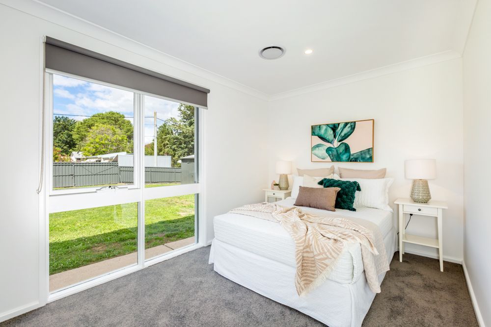 Bedroom with a bed, nightstands, and a large window overlooking a yard.