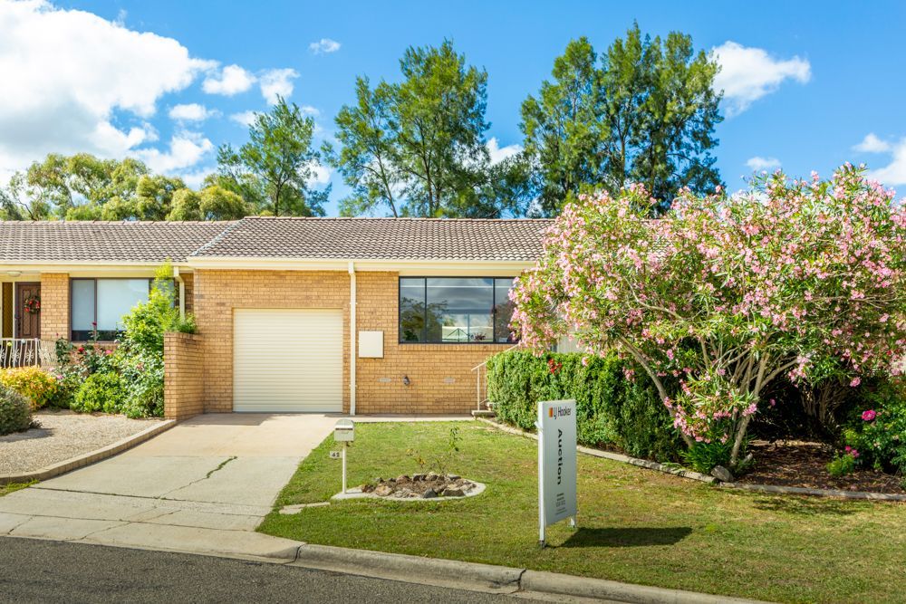 A beige brick townhouse with a garage, windows, and lush green lawn under a partly cloudy sky.