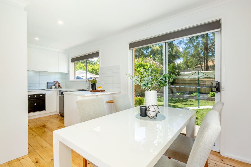 White kitchen and dining area with sliding glass door to backyard. Bright, modern decor.