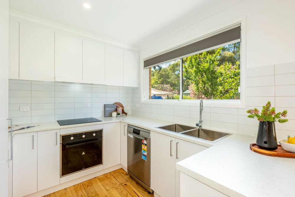White kitchen with stainless steel appliances, window, and wooden floor.