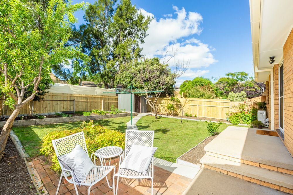 Backyard with lawn, patio furniture, and brick steps leading to a house under a blue sky.