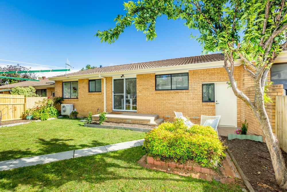Brick home with small yard, green grass, and trees under a blue sky.
