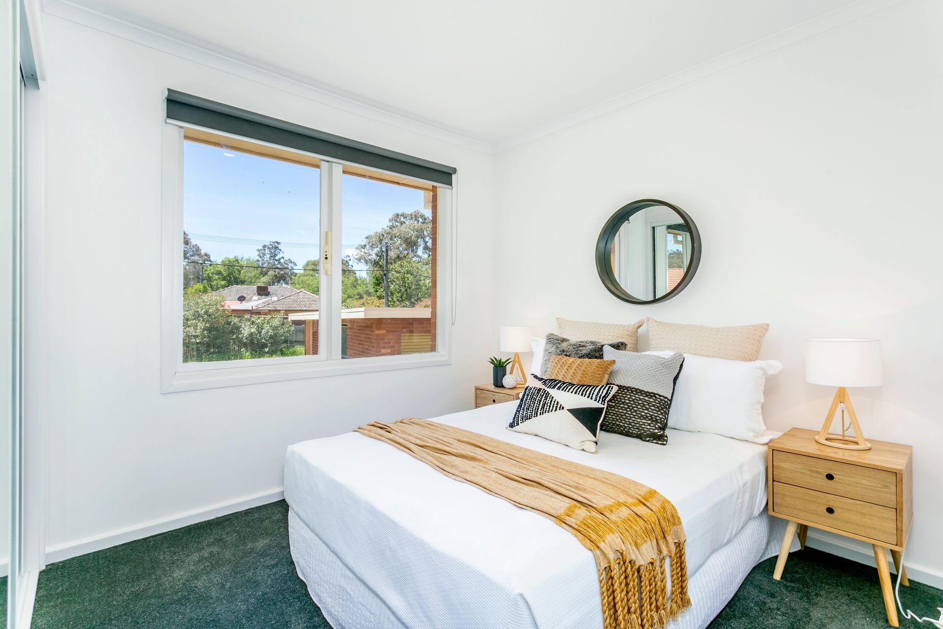 Bedroom with double bed, nightstand, window, mirror, and green carpet.