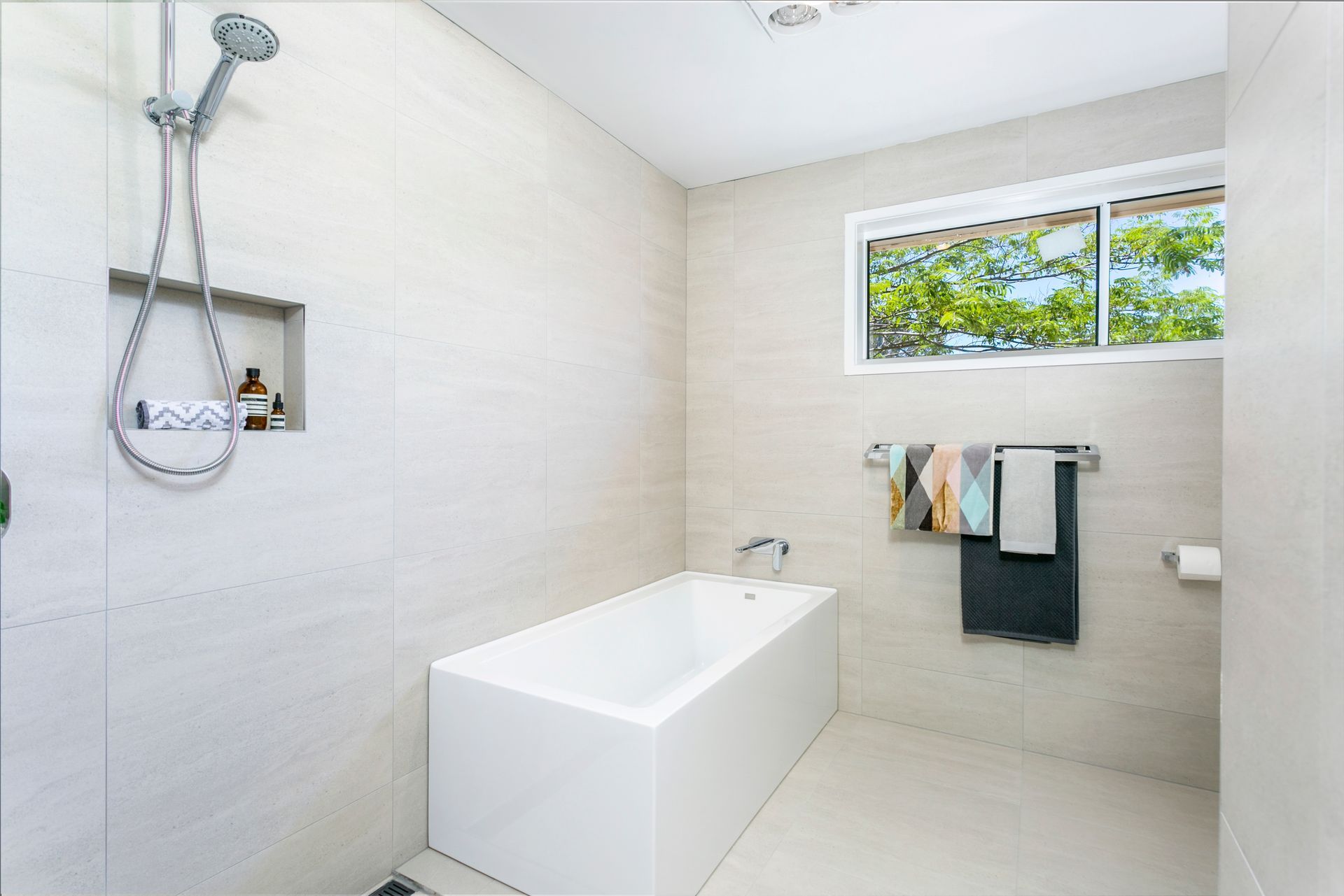 Modern bathroom with a bathtub, shower, window, and neutral-toned tiles.