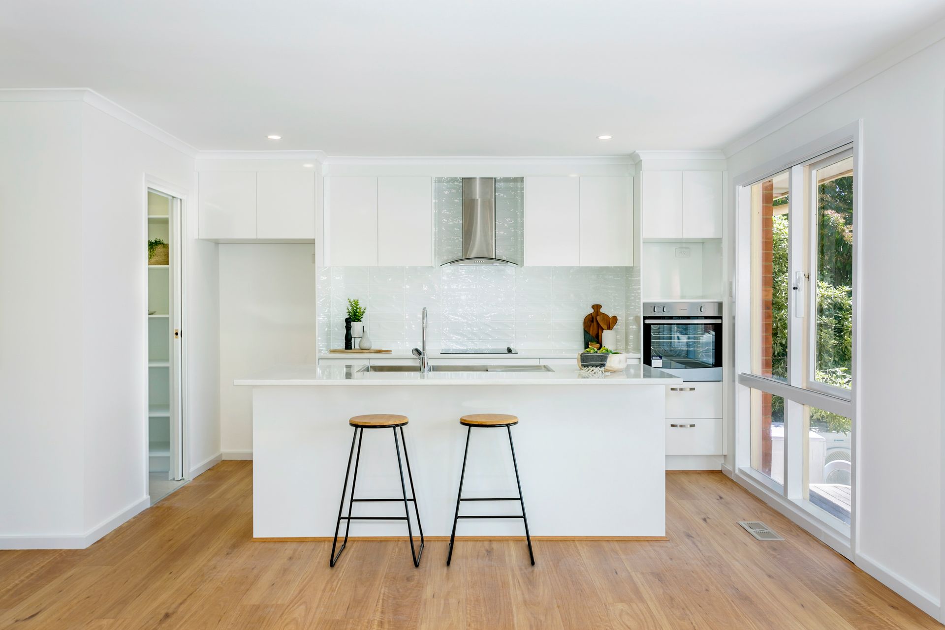 White modern kitchen with island and two stools. Wood floors and large windows.