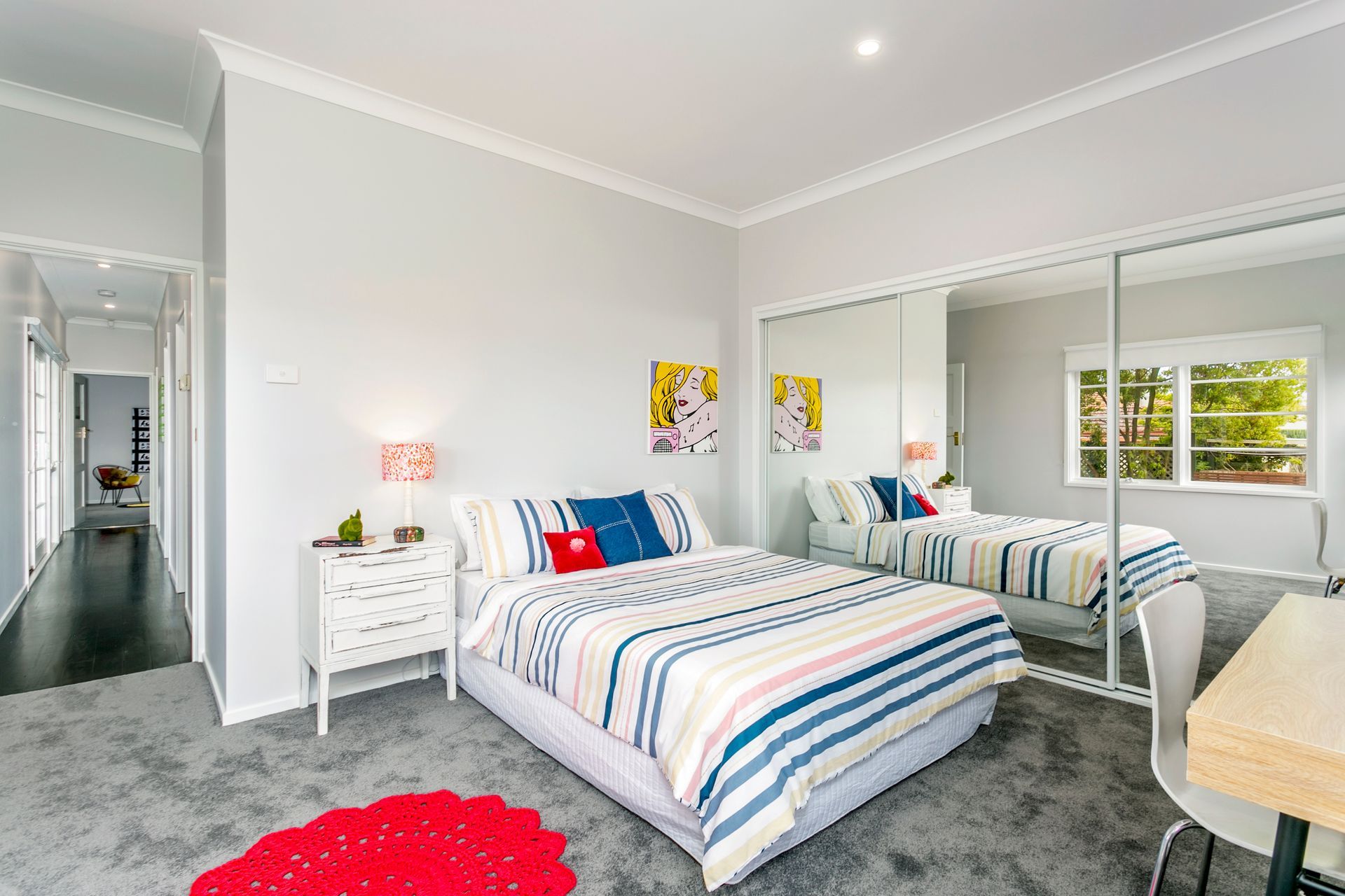 Bedroom with bed, mirrored closet doors, and a small desk. Gray carpet and walls; colorful bedding.