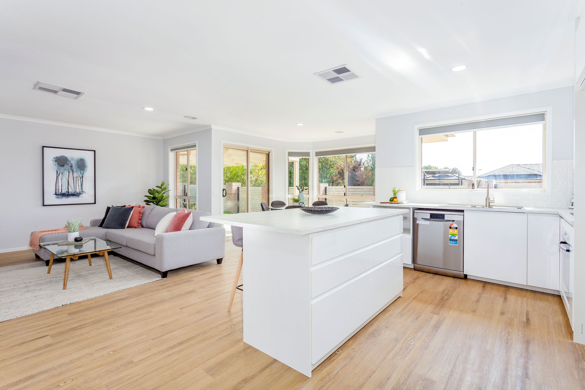 Open-plan kitchen and living area with white cabinetry, island, light wood flooring, and gray sofa.