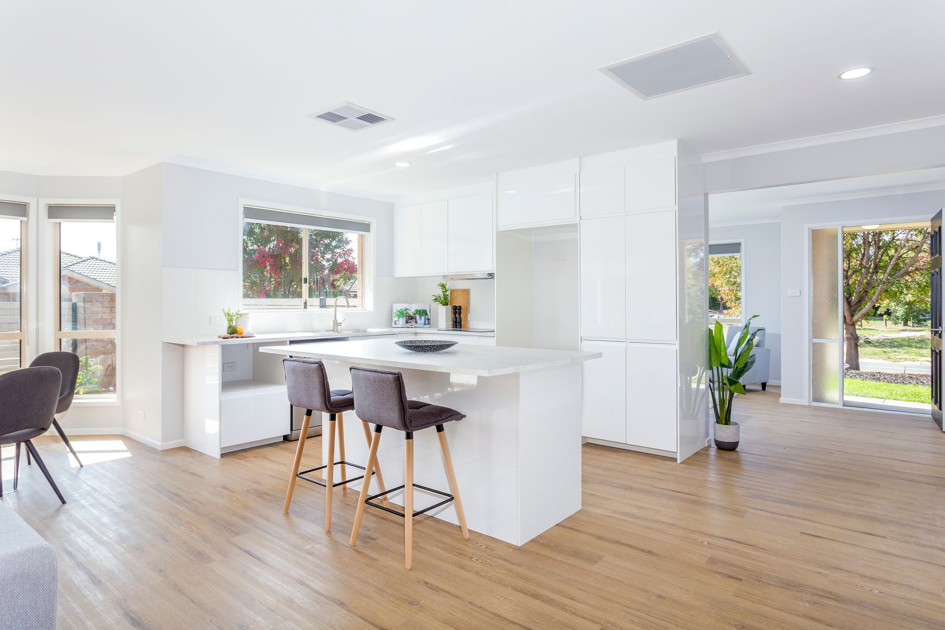 Bright kitchen with white cabinetry, island with bar stools, and wooden flooring.