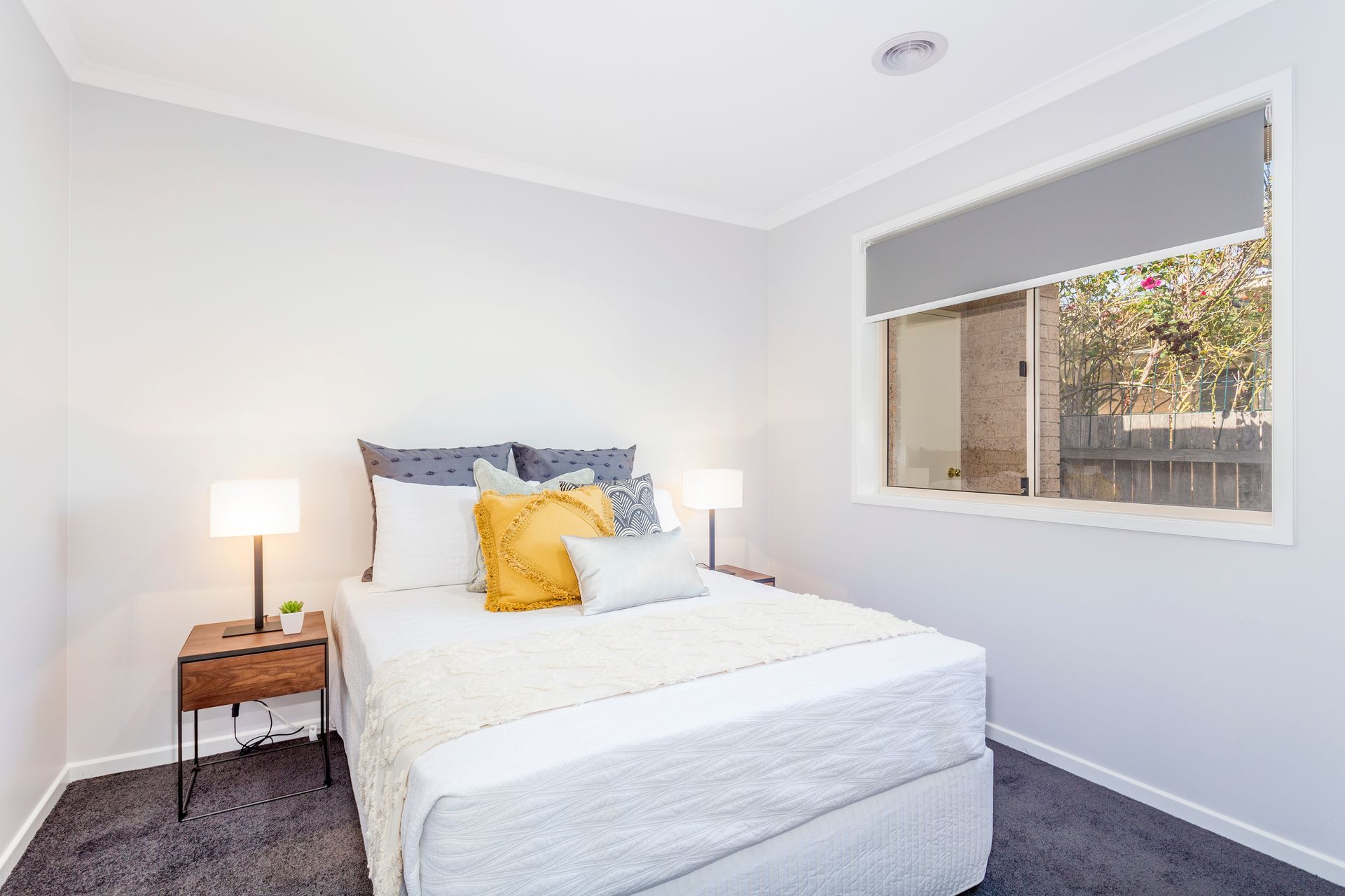 Bedroom with gray walls, bed with pillows, nightstands, and window with a shade.