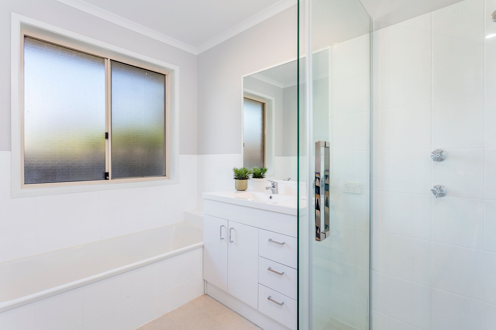 White bathroom with a frosted window, vanity, mirror, shower, and tub.