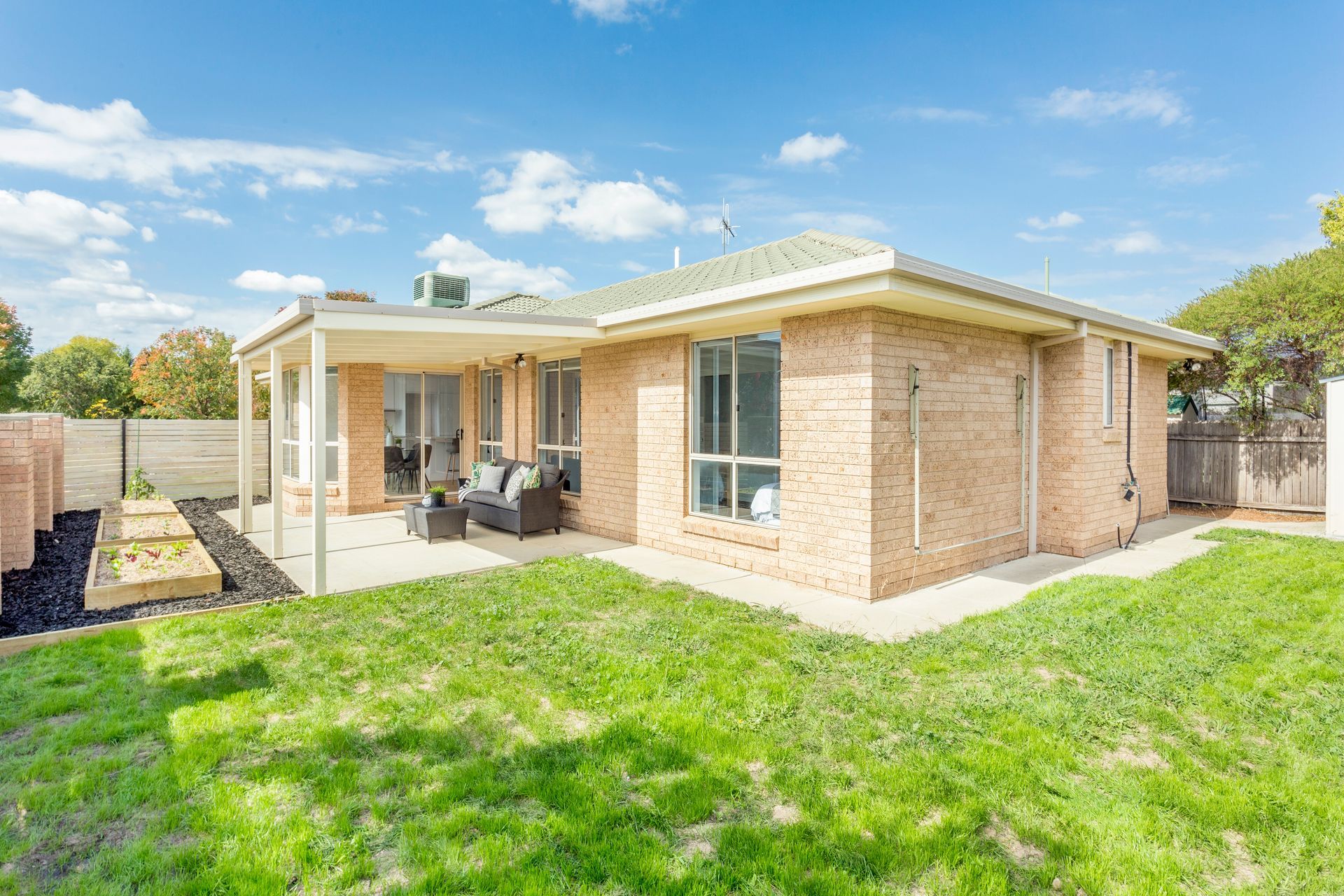 Brick house with covered patio, green lawn, blue sky.