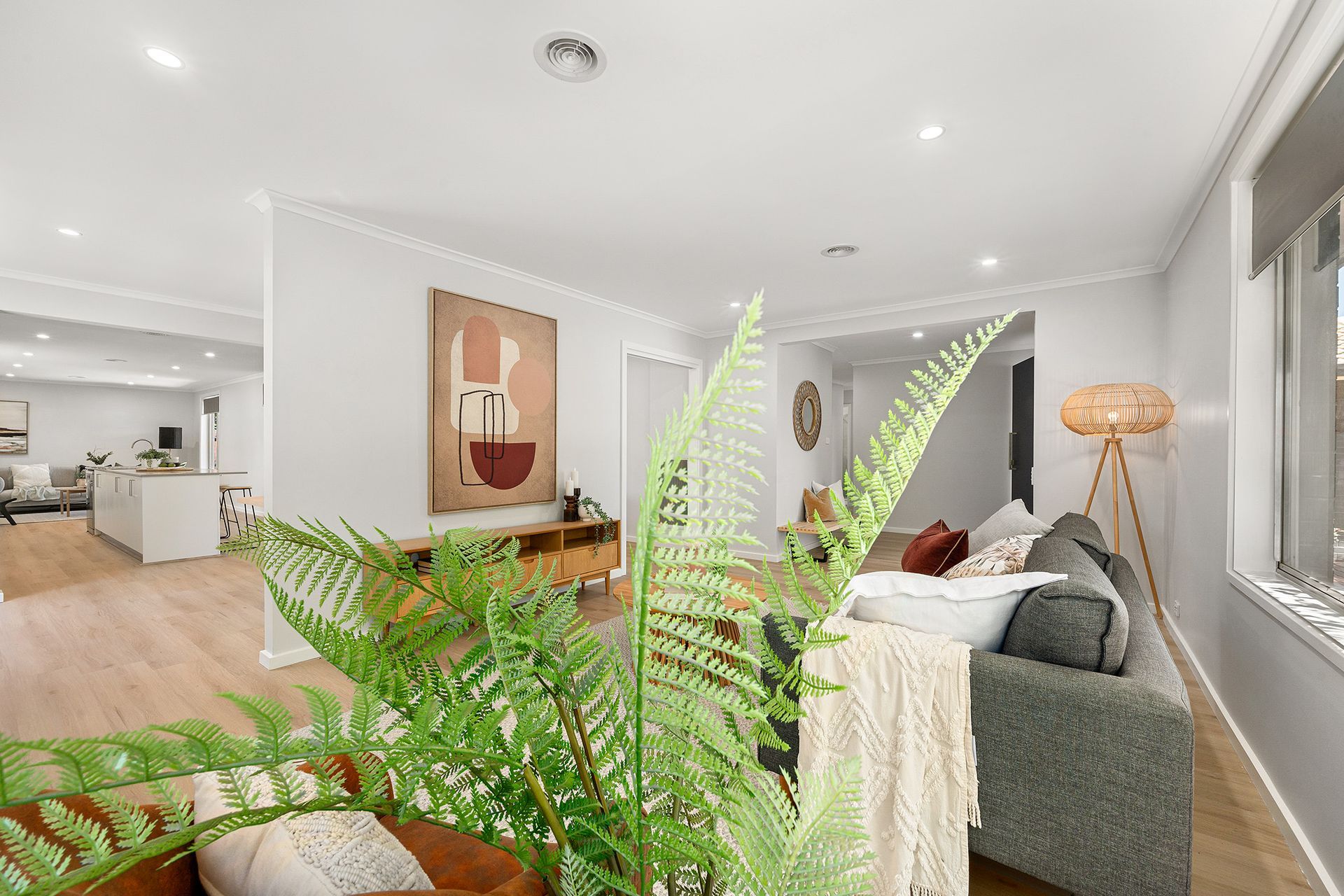 Living room with fern in foreground, gray sofa, art on wall, and view of kitchen.