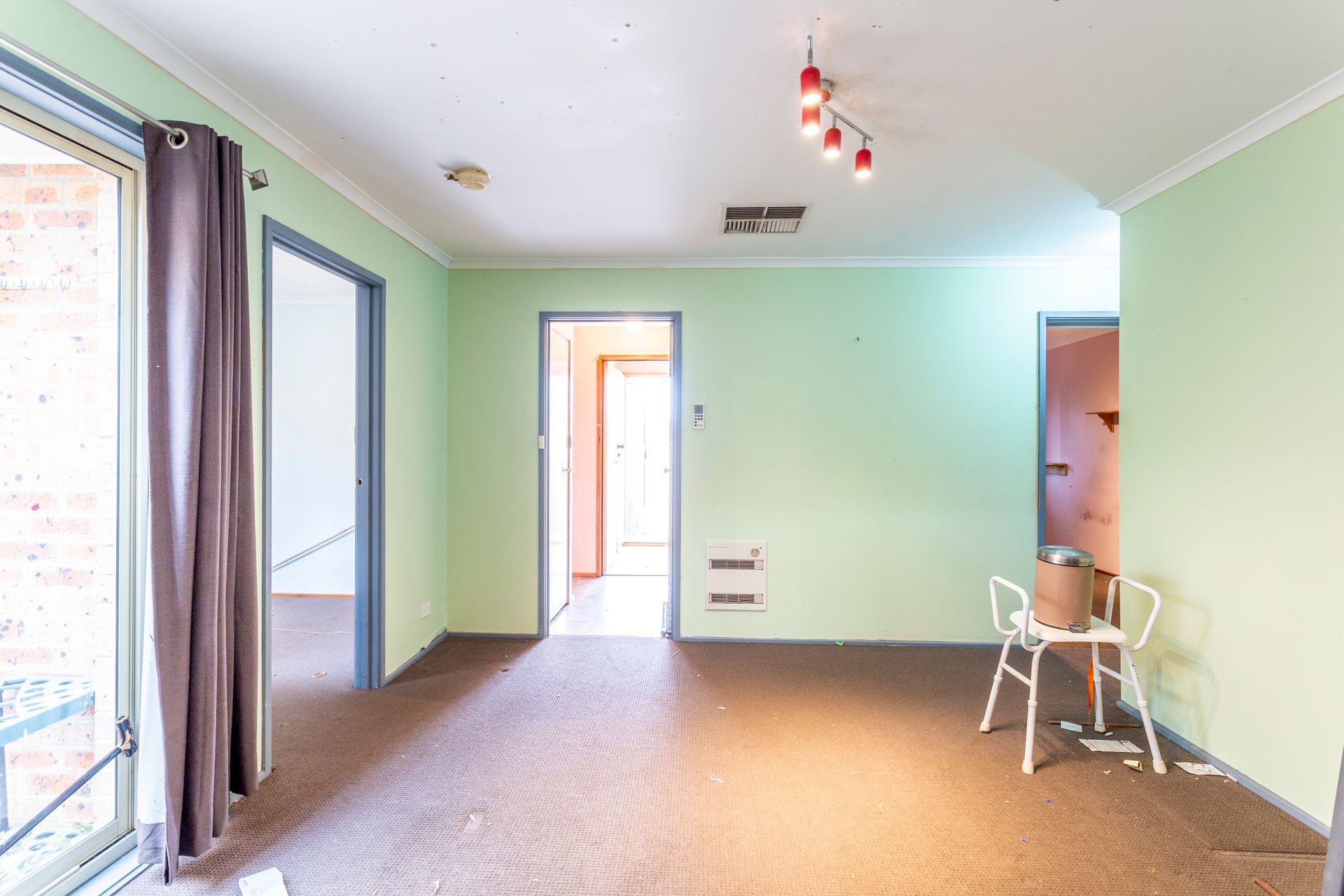 Empty interior room with light green walls, brown carpet, and three open doorways.
